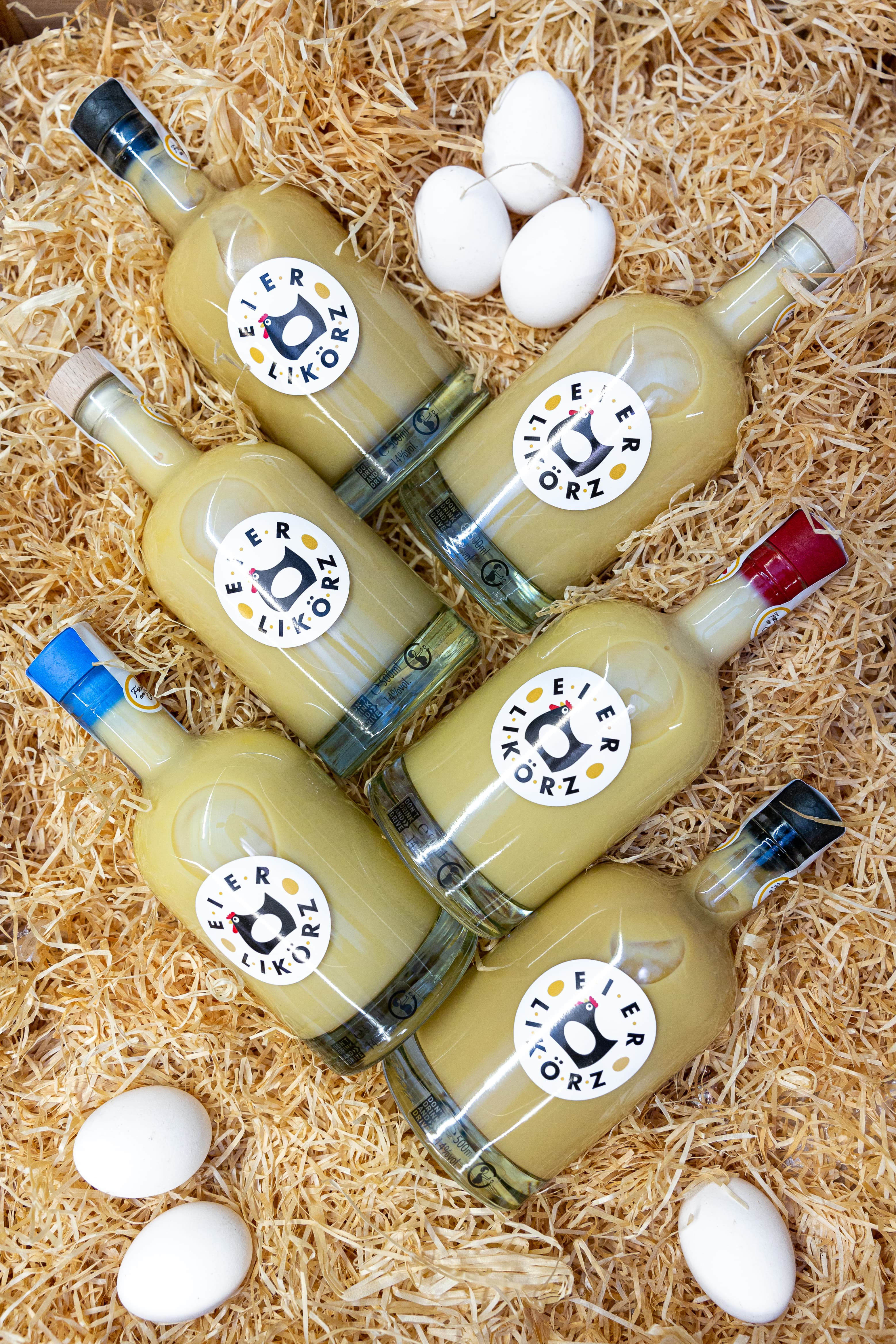 Sechs Flaschen Eierlikör auf Stroh drapiert.