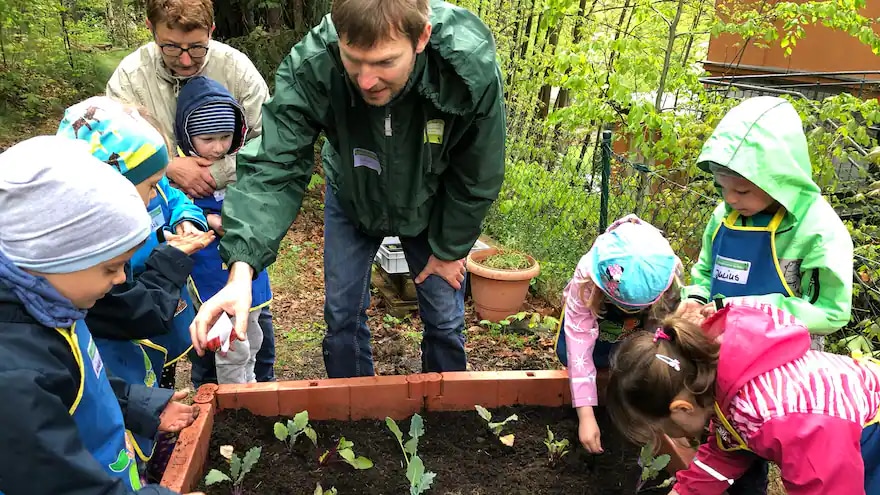 Einige Kinder bepflanzen ein Hochbeet mit einem Erwachsenen.