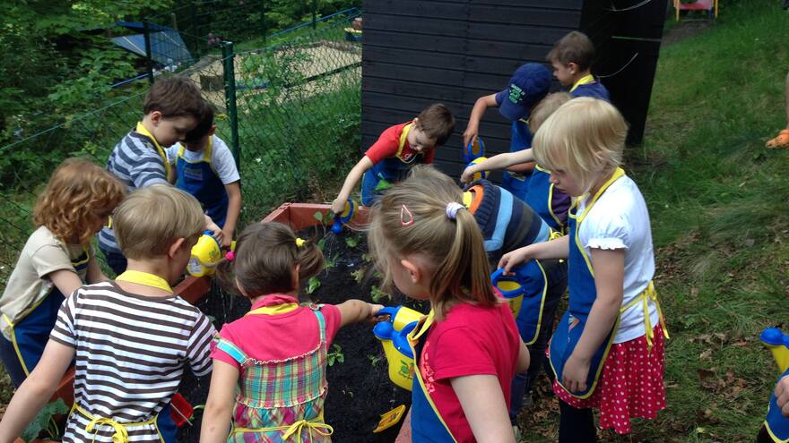 Viele Kinder bepflanzen ausgestattet mit Schürze und Gieskanne eine Hochbeet.