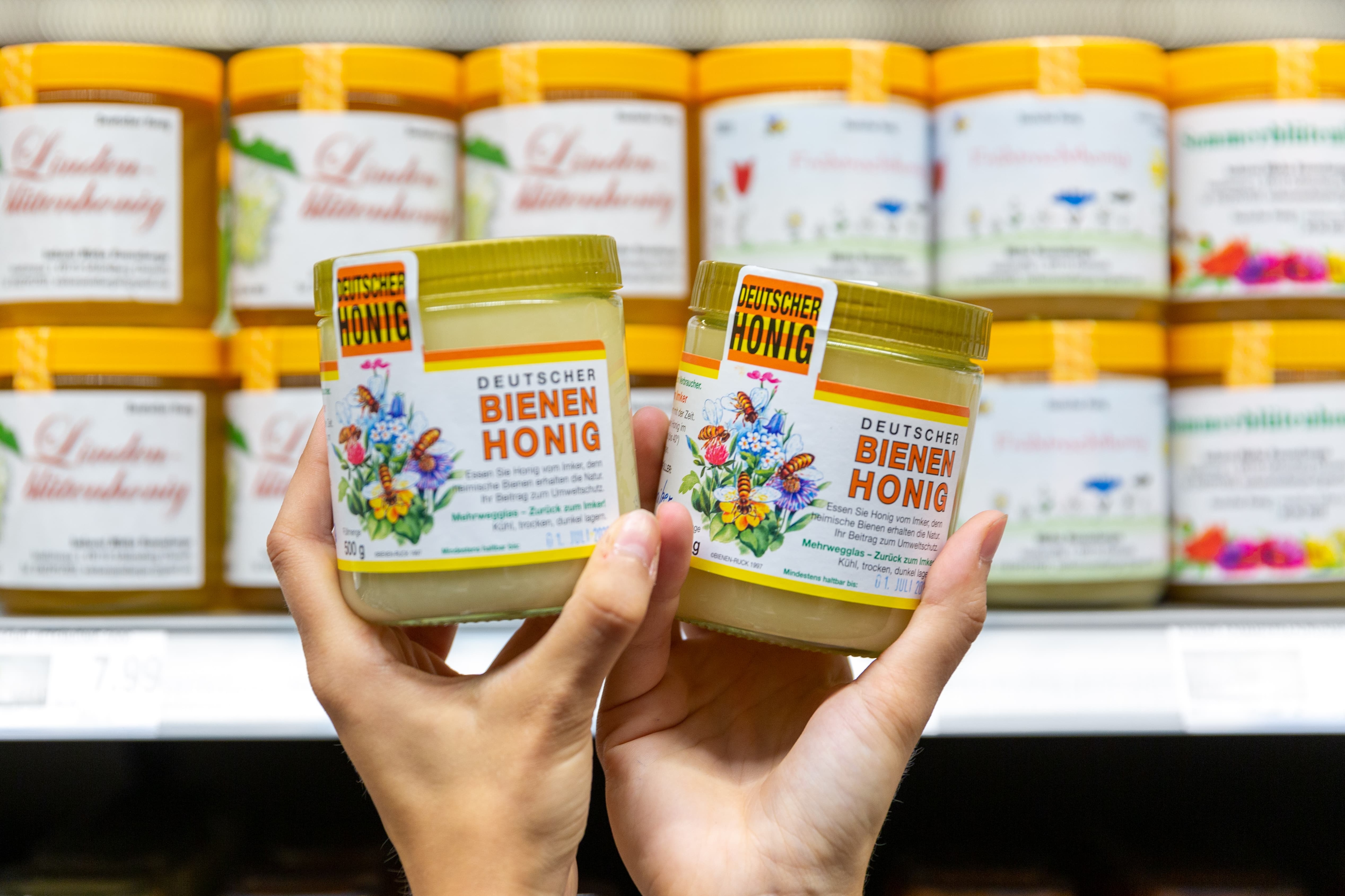 Zwei Hände halten jeweils ein Glas des regionalen Honigs.