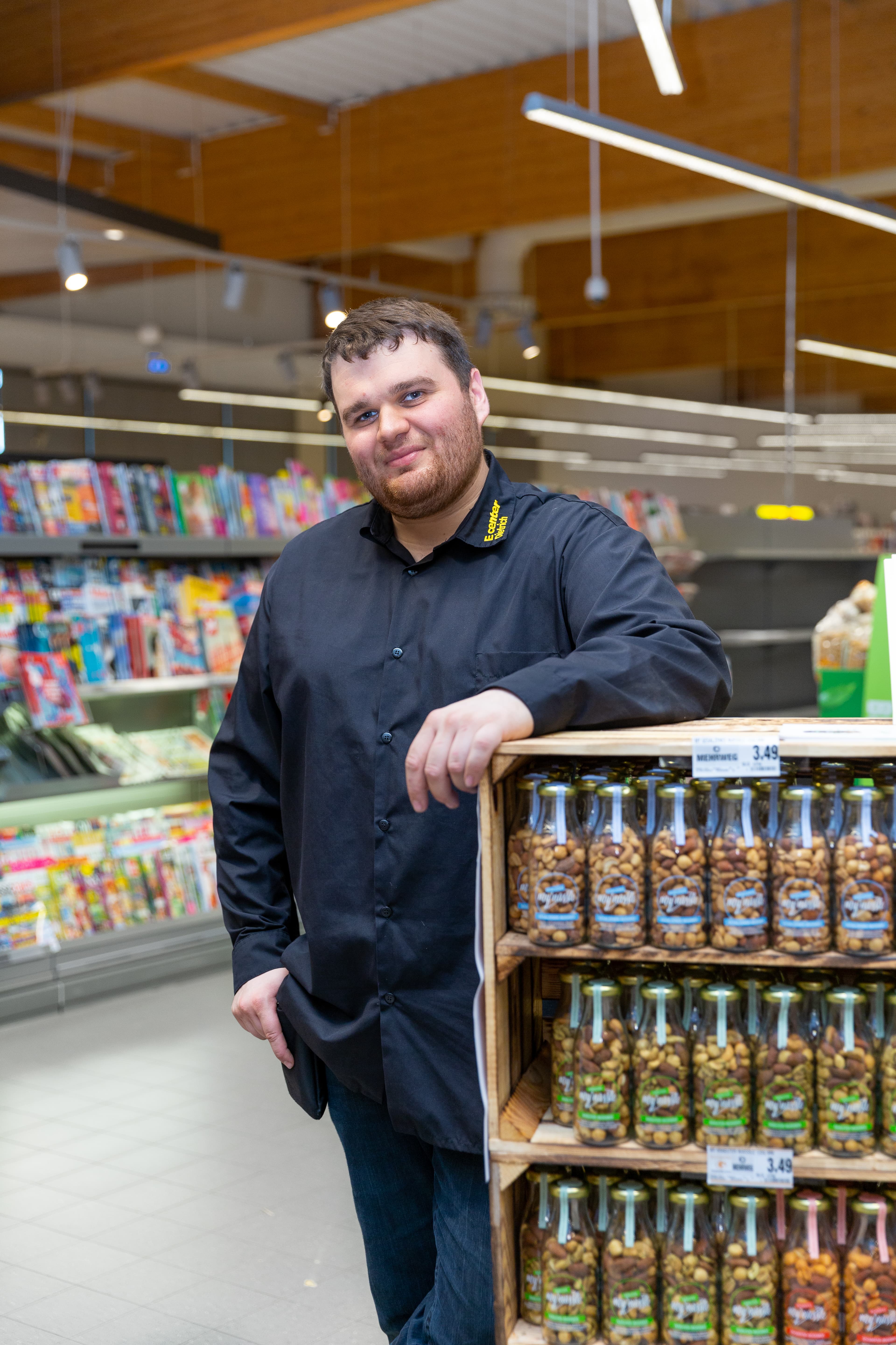Ein Mitarbeiter lehnt sich auf einen Aussteller mit Nüssen und lächelt in die Kamera.