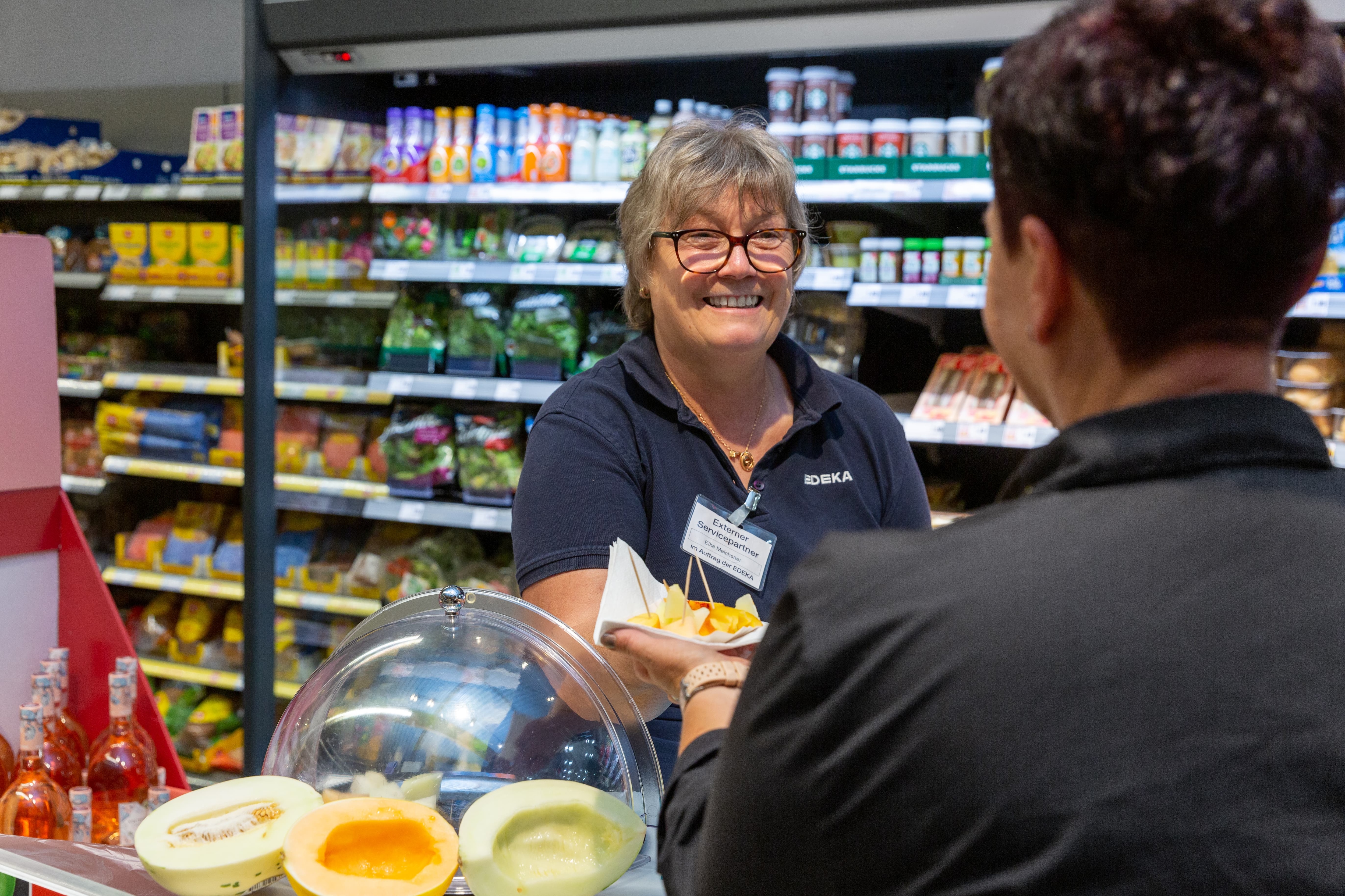 Eine Mitarbeiterin gibt einer Kundin Stücke verschiedener Melonen zum probieren.