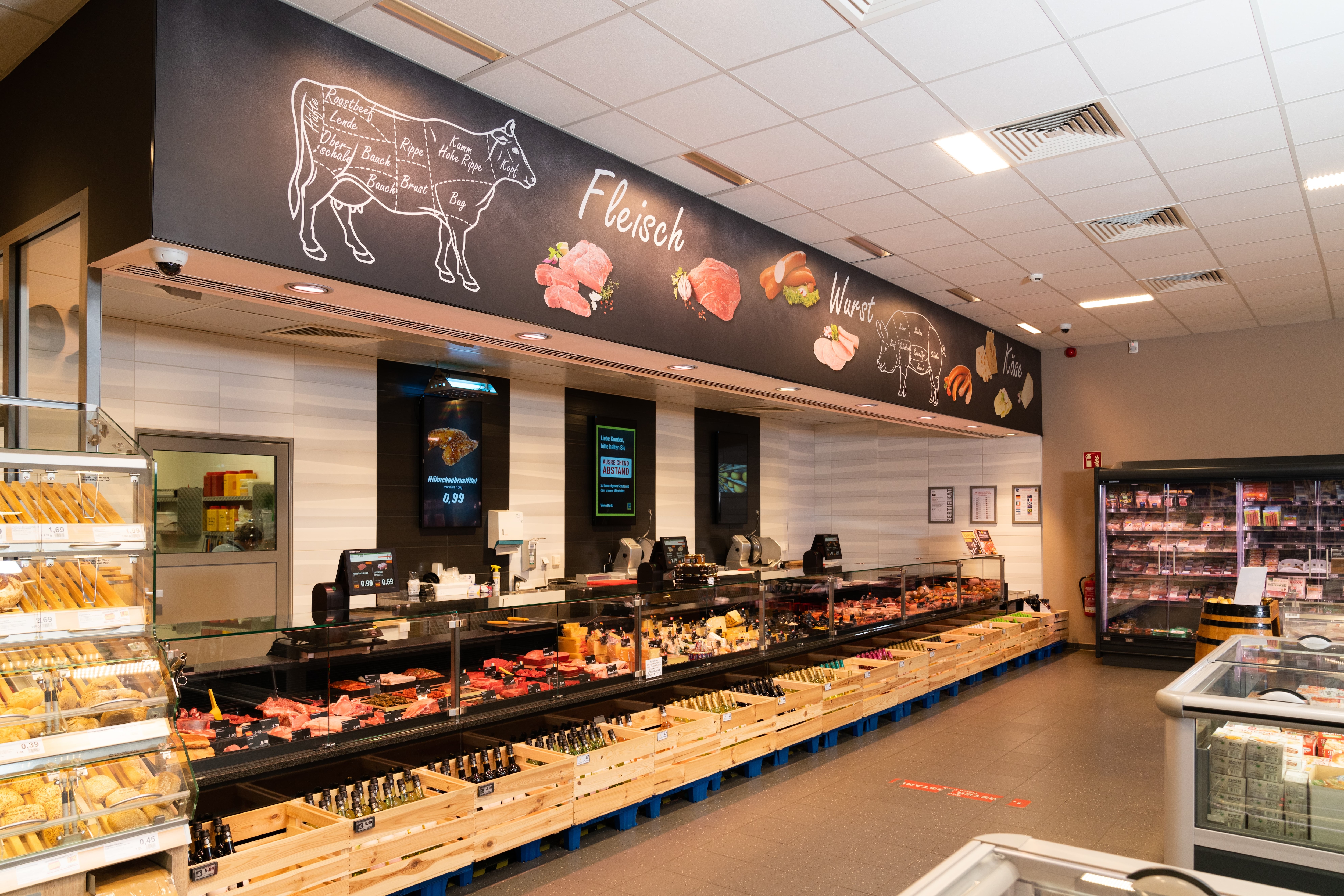 Menschenleere Fleischtheke eines Supermarktes. UNter den Lichtern Illustrationen von Kuh und Schwein.