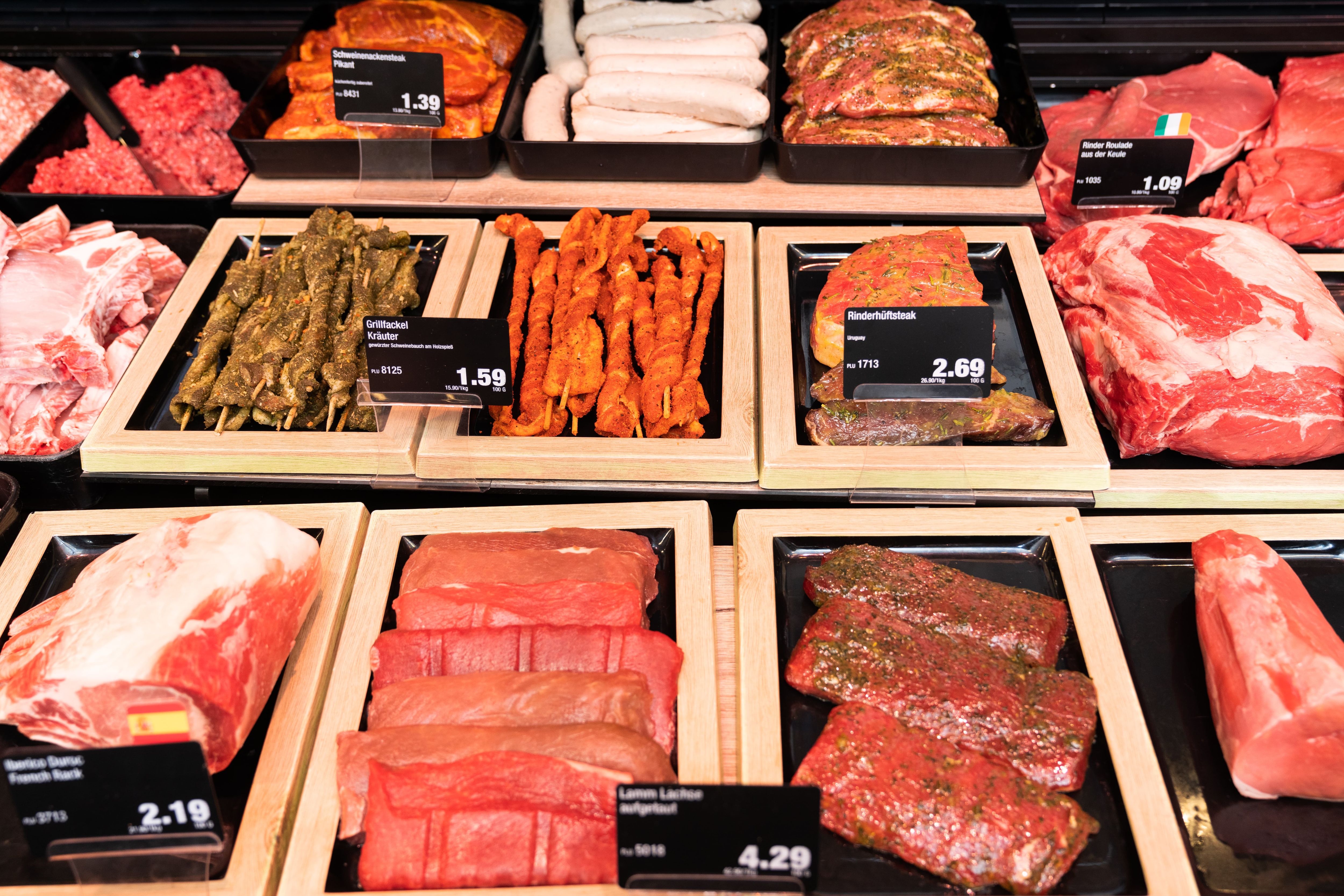 Verschiedene marinierte Fleischsorten und Wurst mit Preisschildern in einer Auslage.