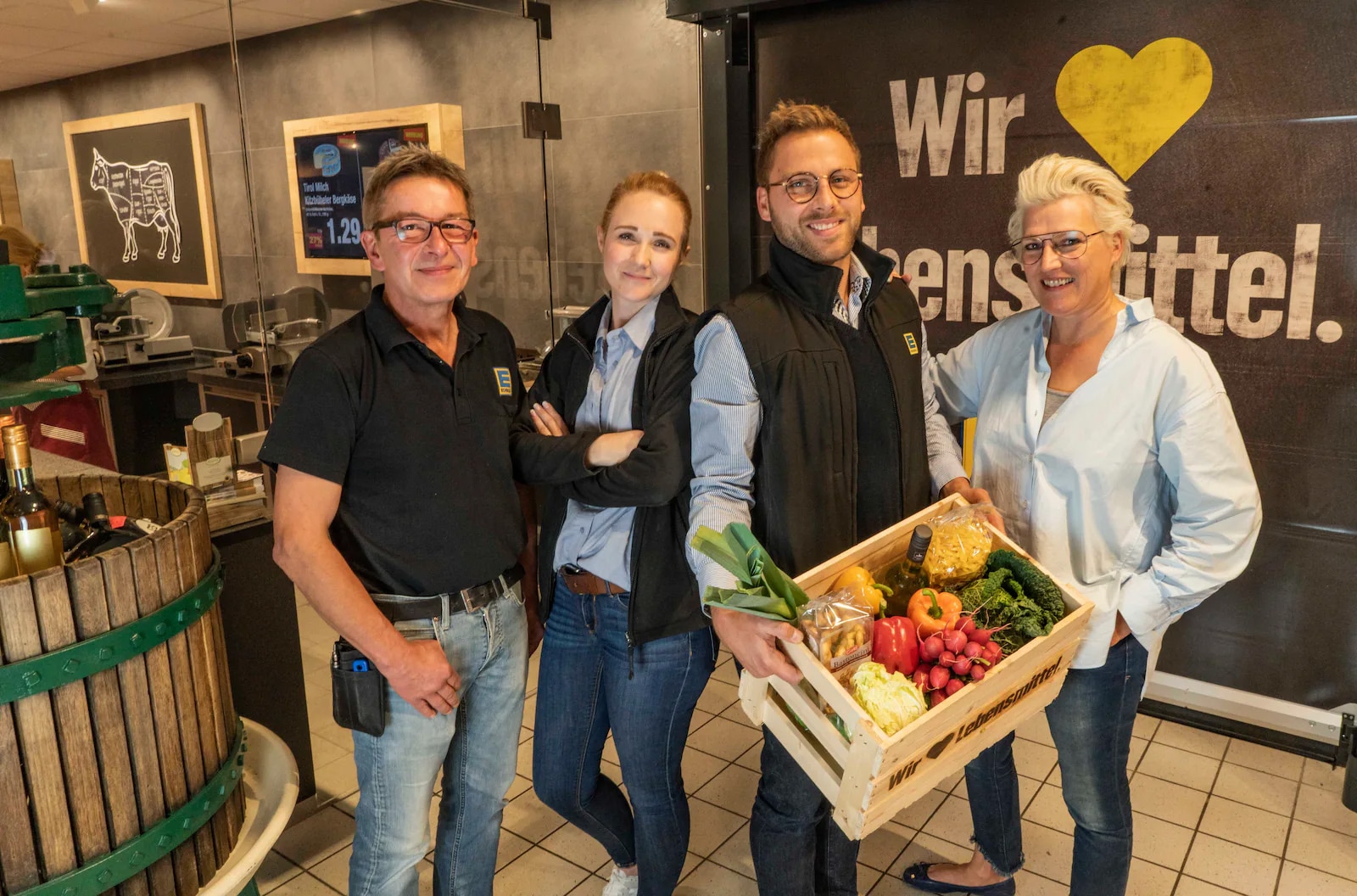 Zwei Männer und zwei Frauen stehen vor der Freischetheke. Der Mann hält eine Kiste mit Gemüse in der Hand.