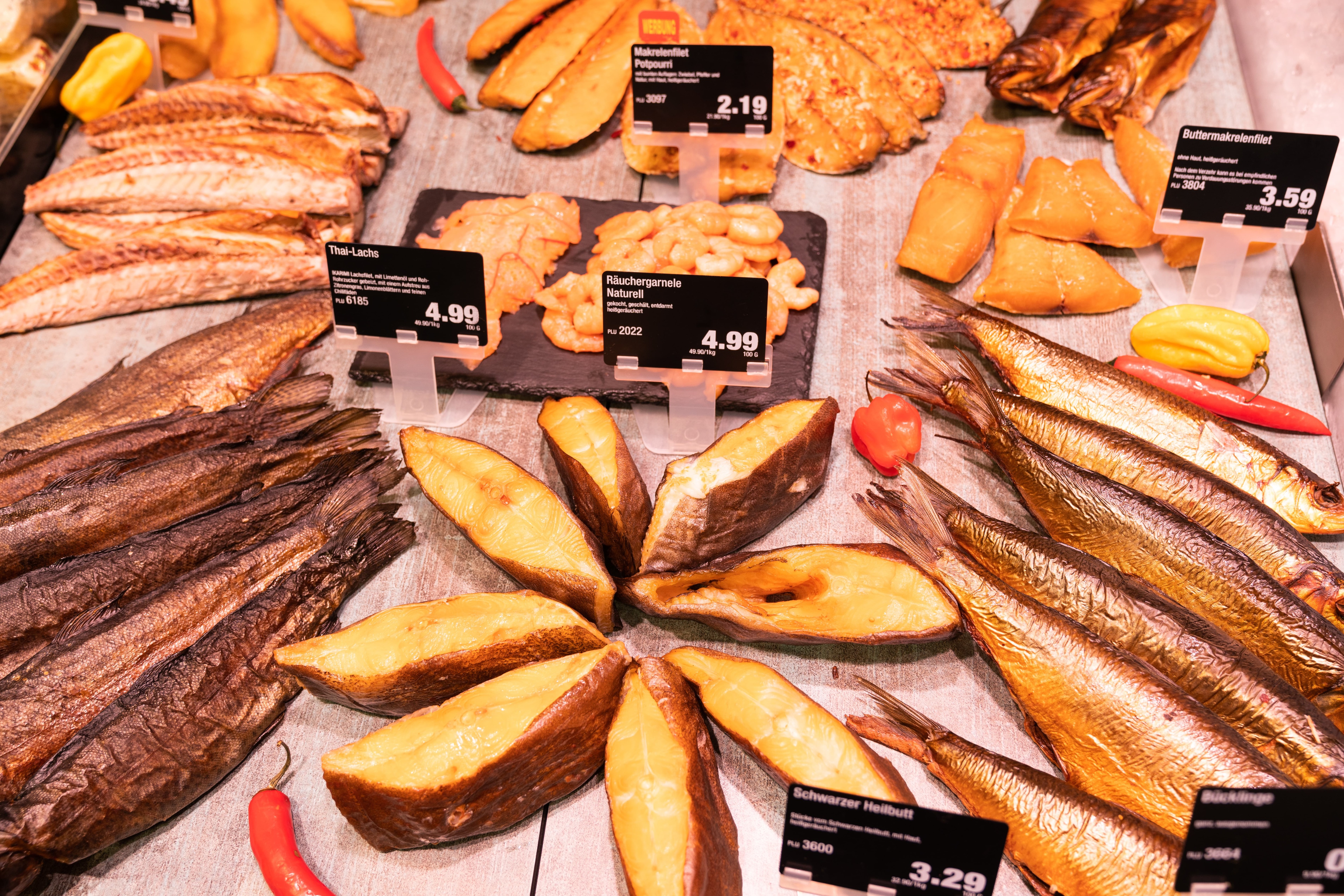 Verschiedene Sorten Räucherfisch in einer Auslage mit Preisschildern.