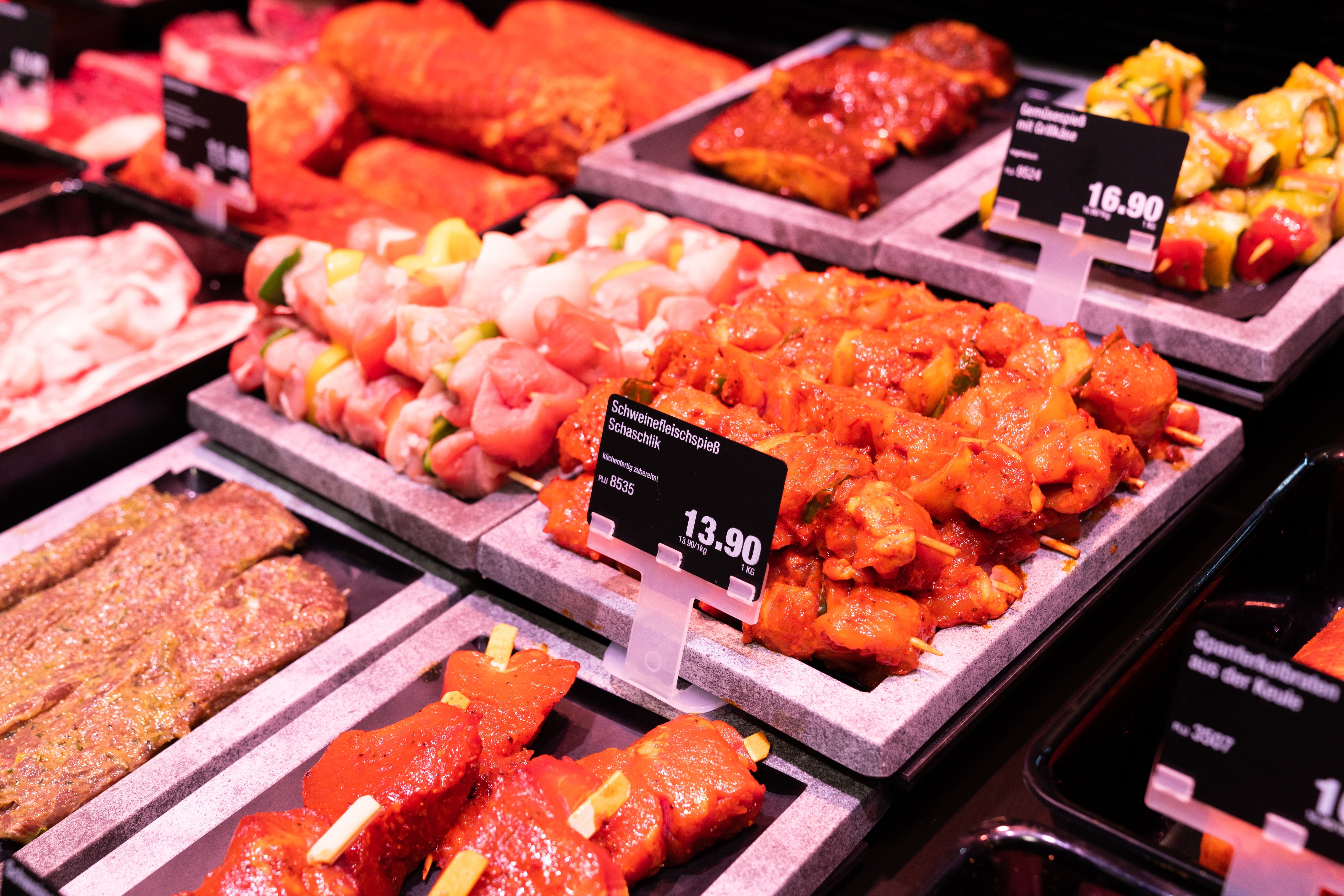 Verschiedene marinierte Fleischsspieße mit Preisschildern in einer Auslage.