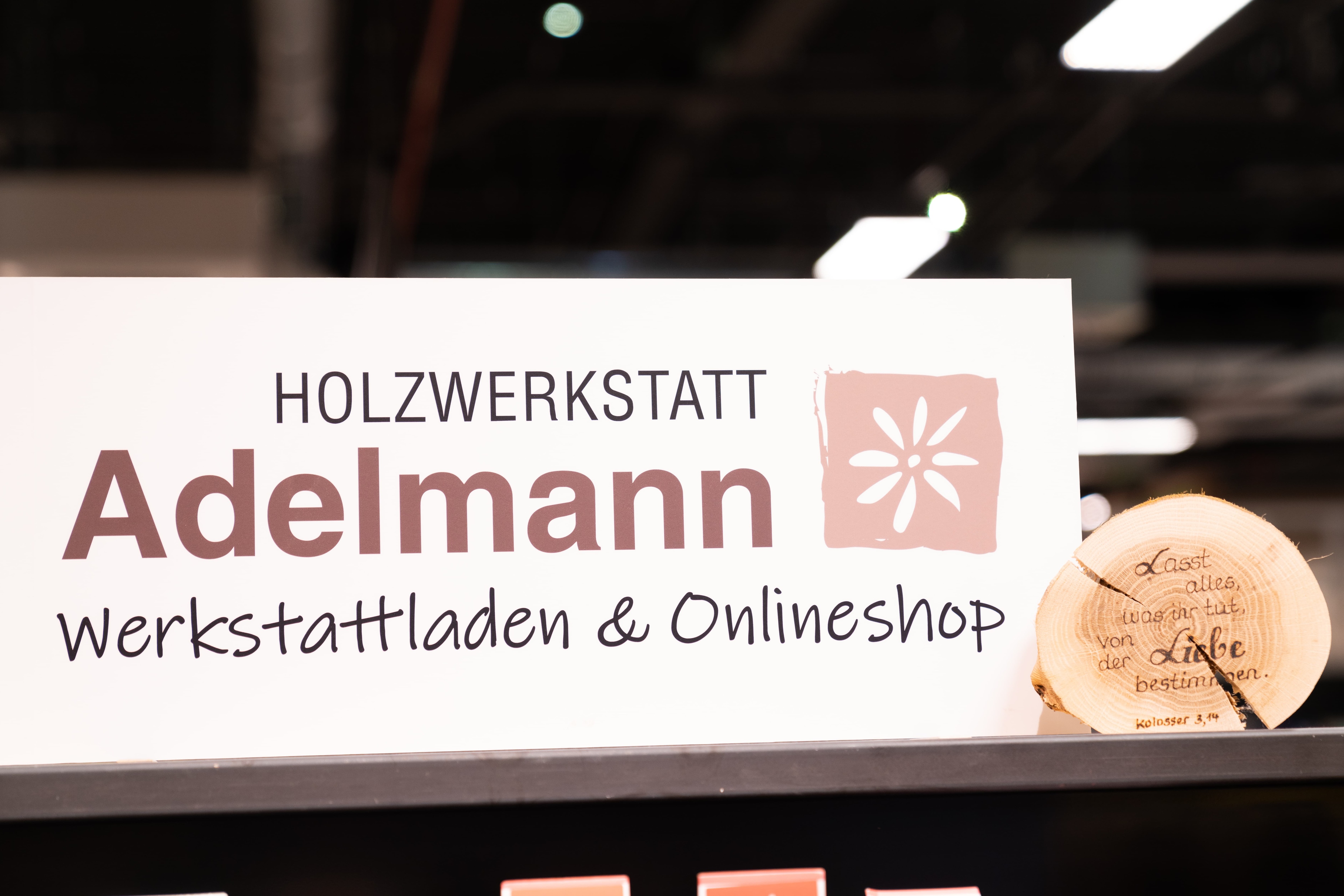 Weißes Schild: Holzwerkstatt Adelmann Werkstattladen und Onlineshop.