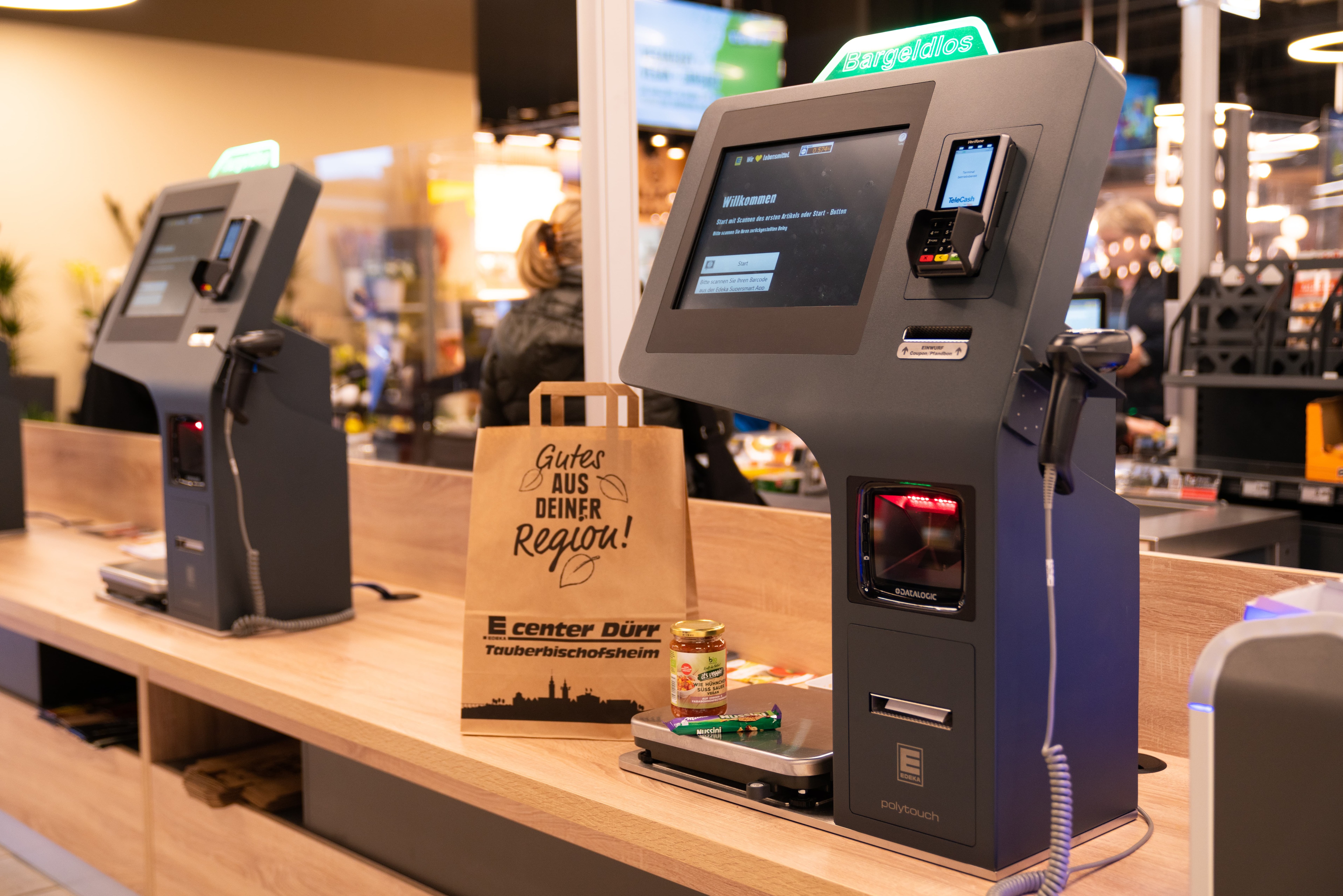 Bargeldlose Selbstbedienungskasse und eine braune Papiertüte mit der Aufschrift Gutes aus der Region. E center Dürr Tauberbischofsheim.