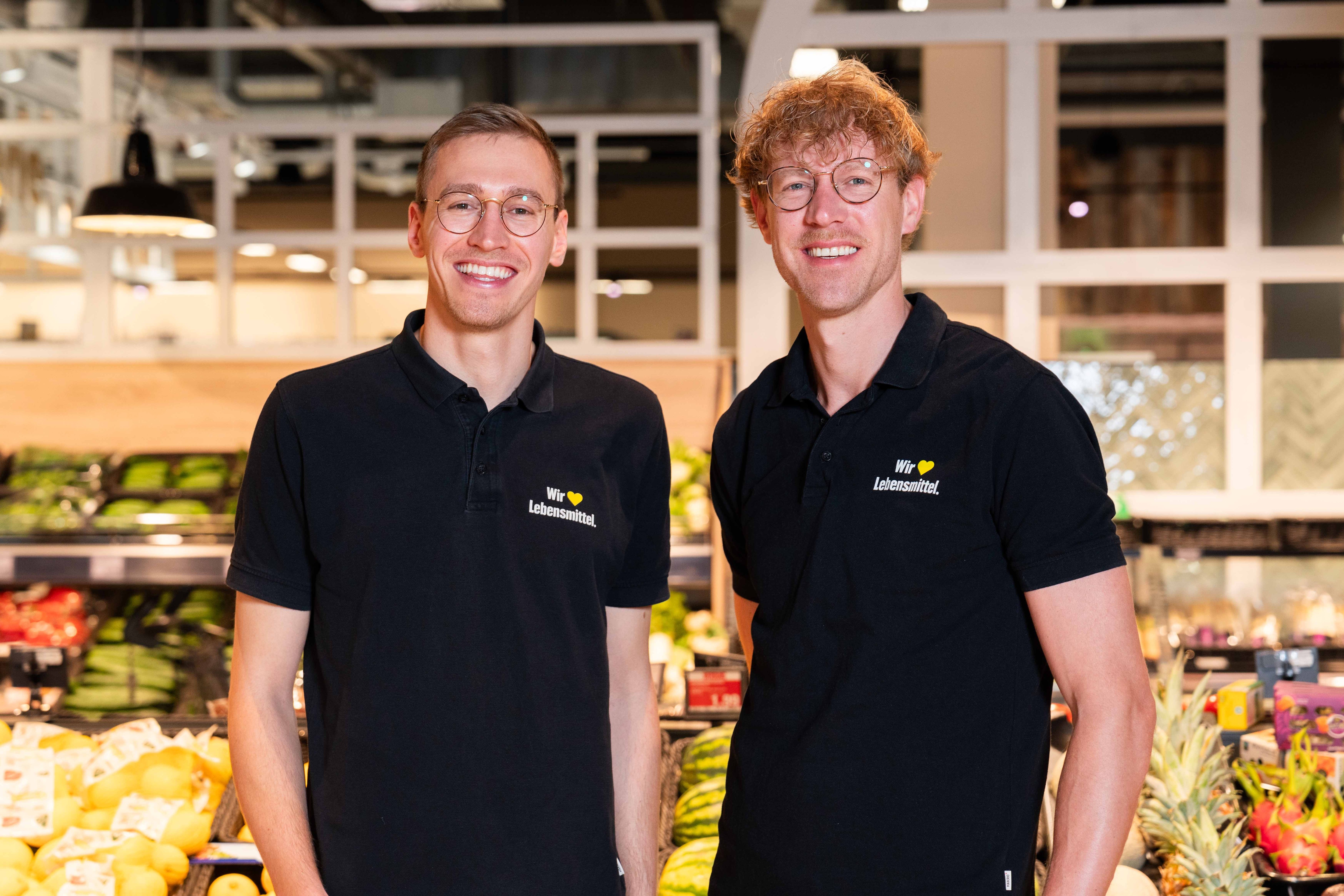 Die Inhaber stehen in der Obst- und Gemüseabteilung in einem EDEKA T-Shirt.