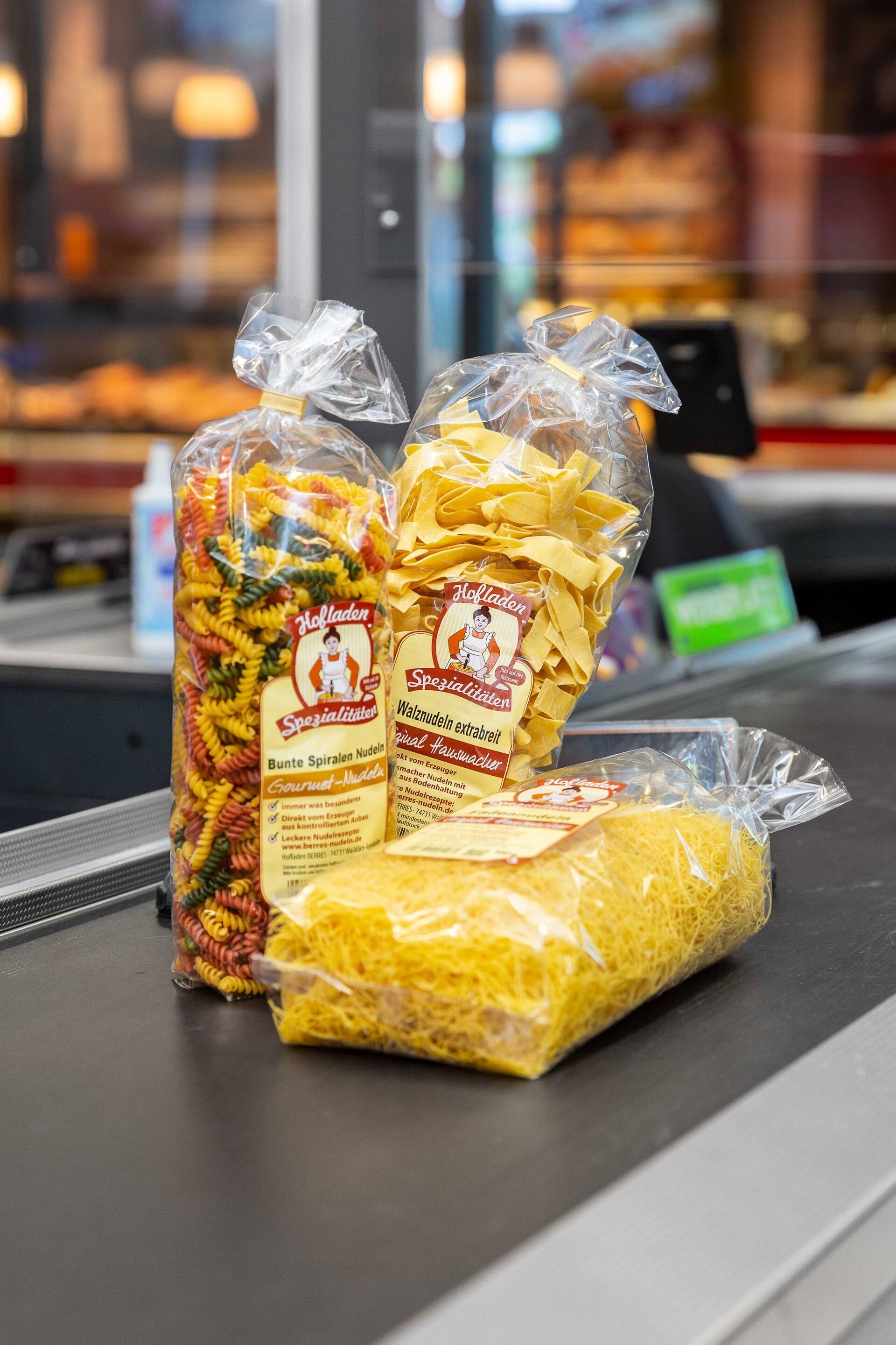 Drei Packungen Nudeln auf einem Kassenband.