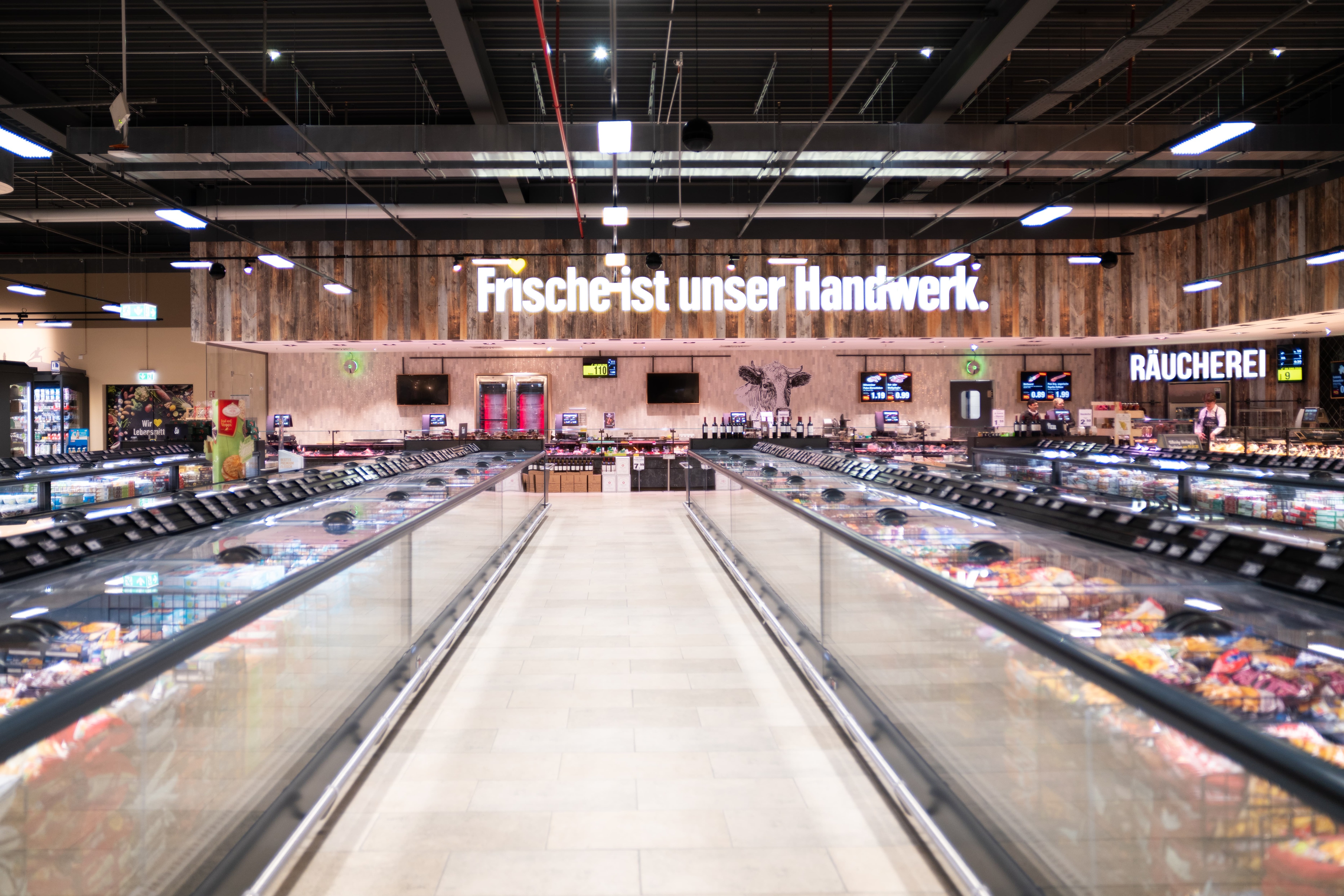 Ein Blick den Gang mit Tiefkühltruhen herunter. Am Ende die Fleischtheke, an der steht: Frische ist unser Handwerk.