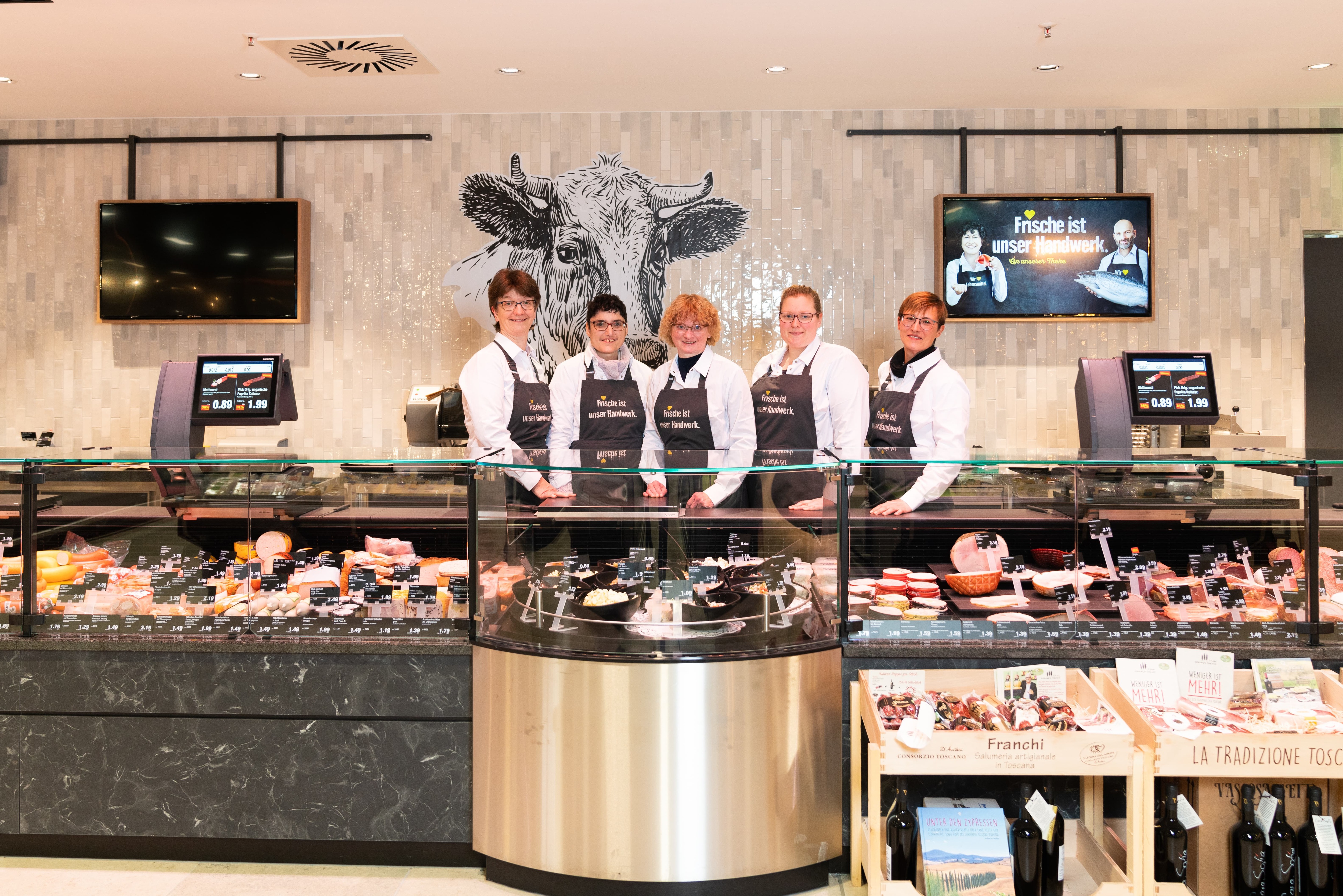 Fünf Personen in weißen Hemden und schwarzen EDEKA-Schürzen stehen hinter dem Tresen für Aufschnitt.