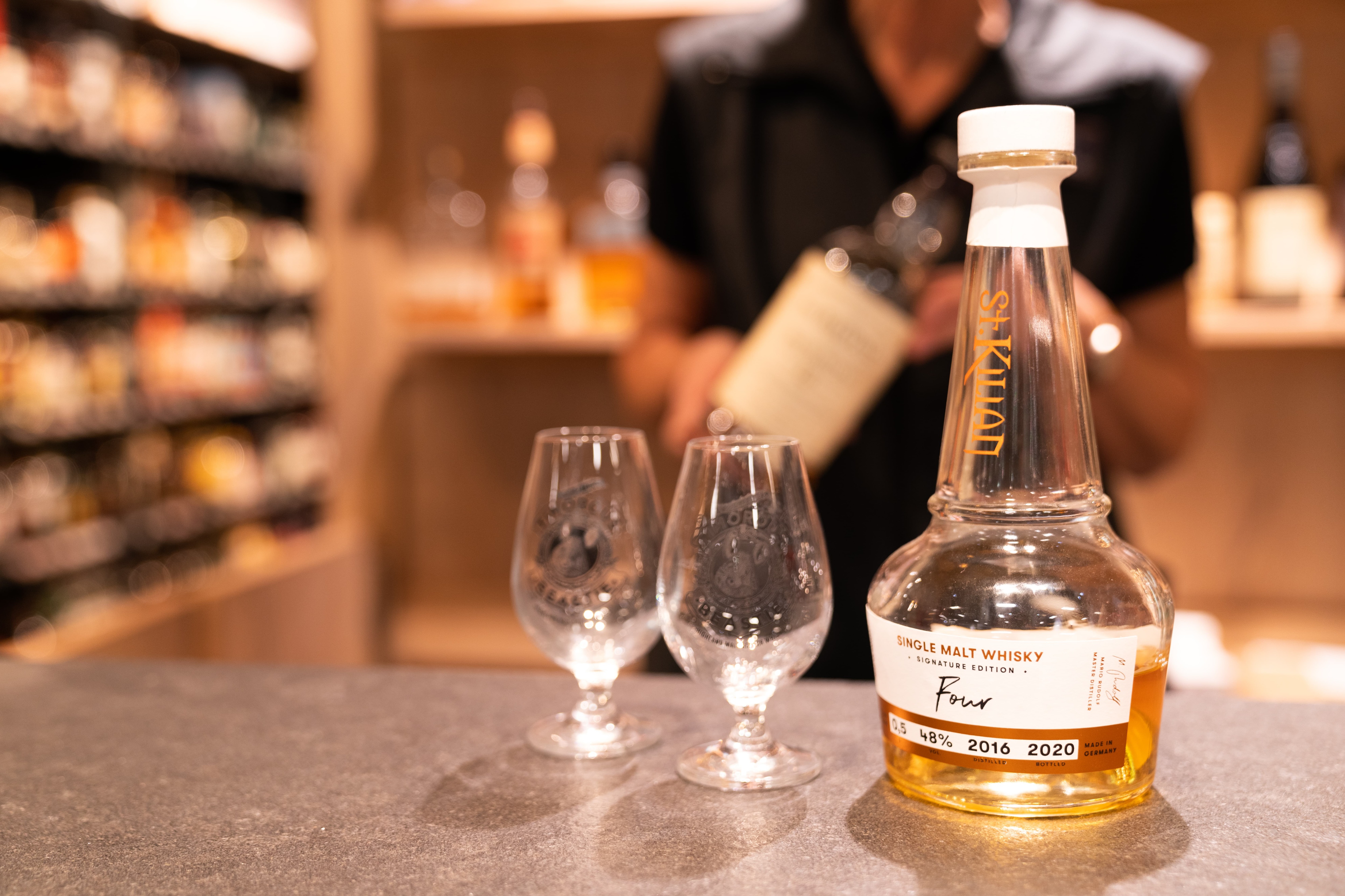 Eine halbgefüllte 0,5 Liter Flasche Single Malt Whisky steht neben zwei kleinen Whisky-Gläsern.