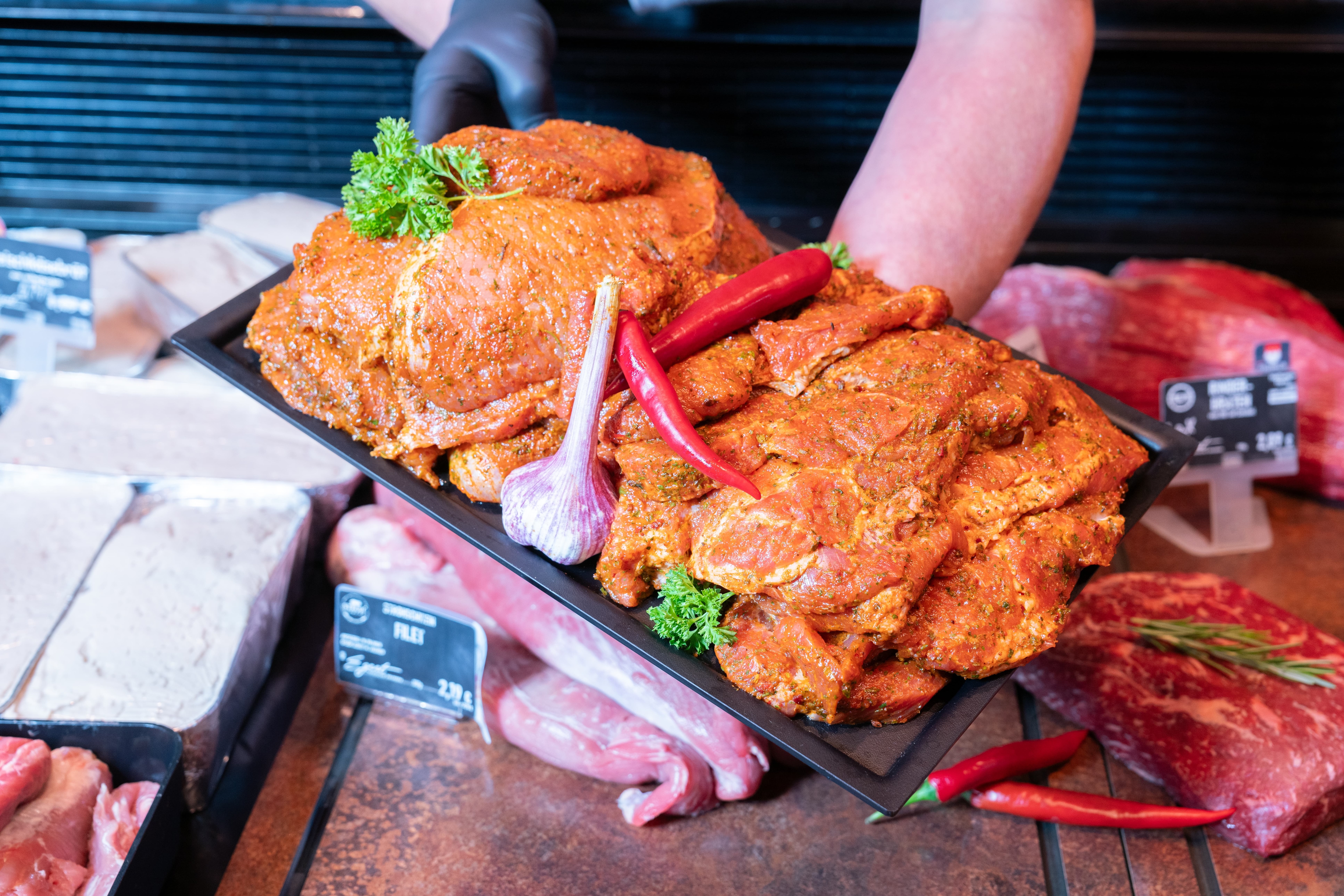 Zwei Hände legen eine Platte mit Fleischstücken die Auslage einer Fleischtheke.