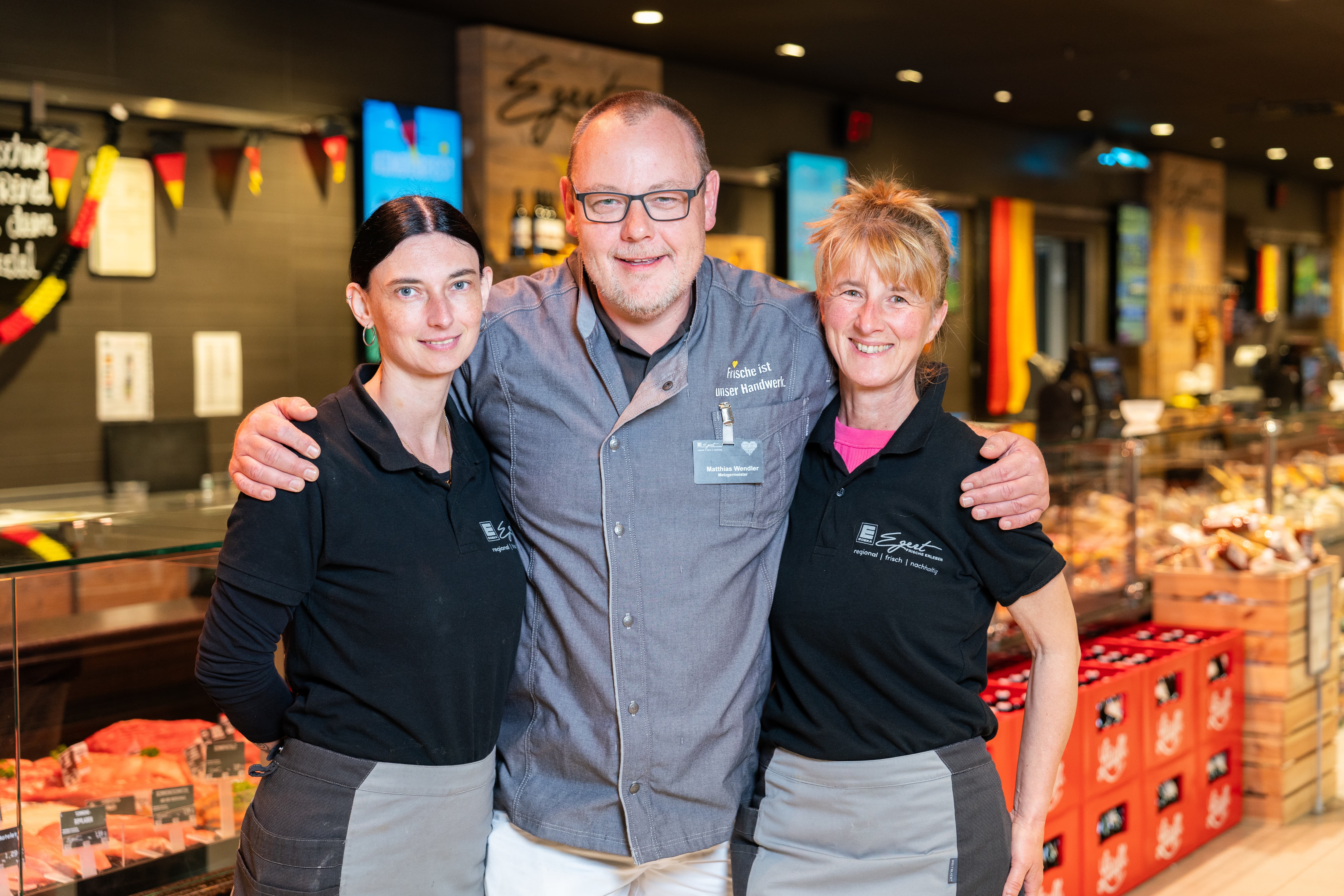 Drei lächelnde Mitarbeitende eines EDEKA-Marktes.