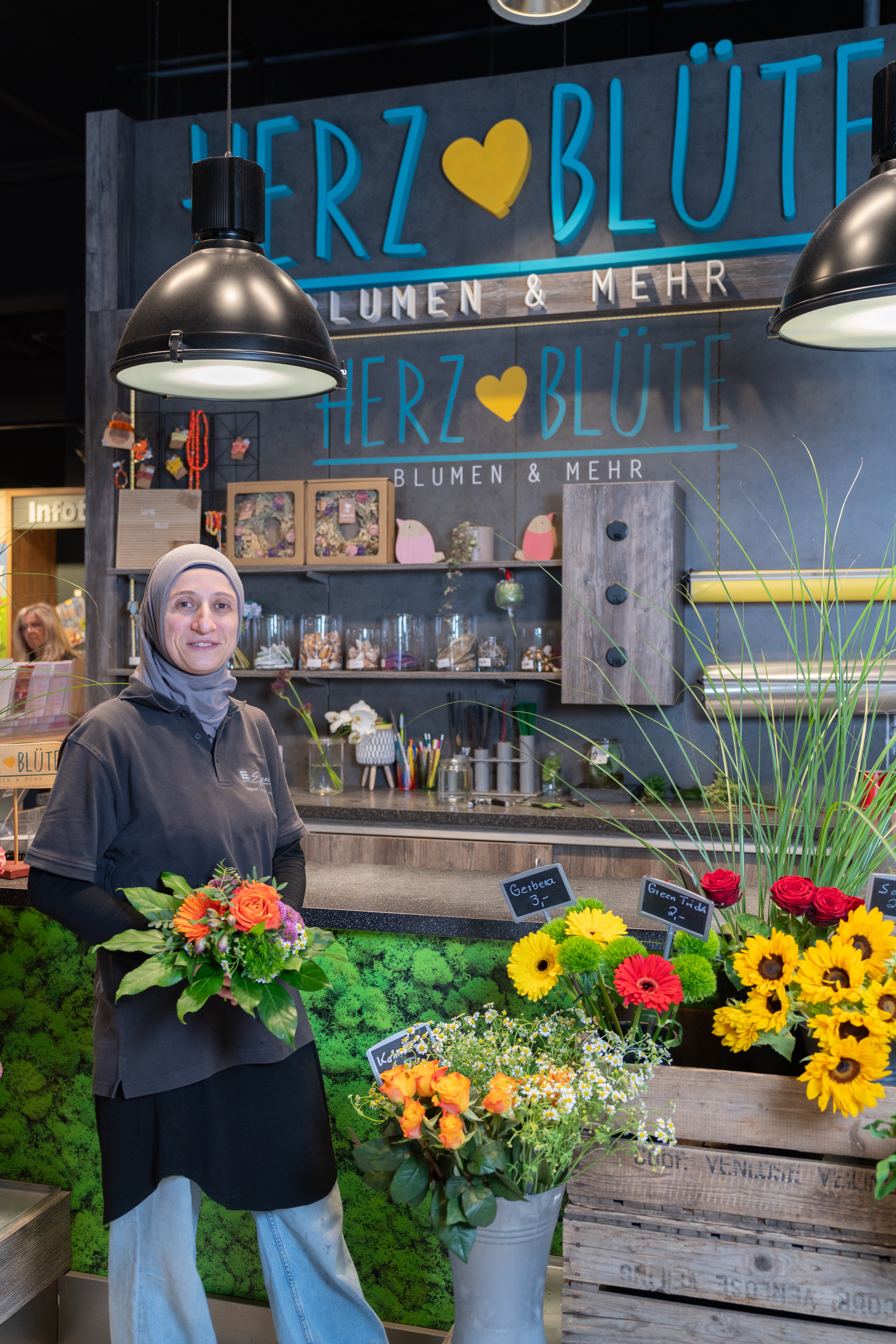 Eine lächelnde Mitarbeiterin eines EDEKA-Marktes hält einen Strauß Blumen in der Hand.