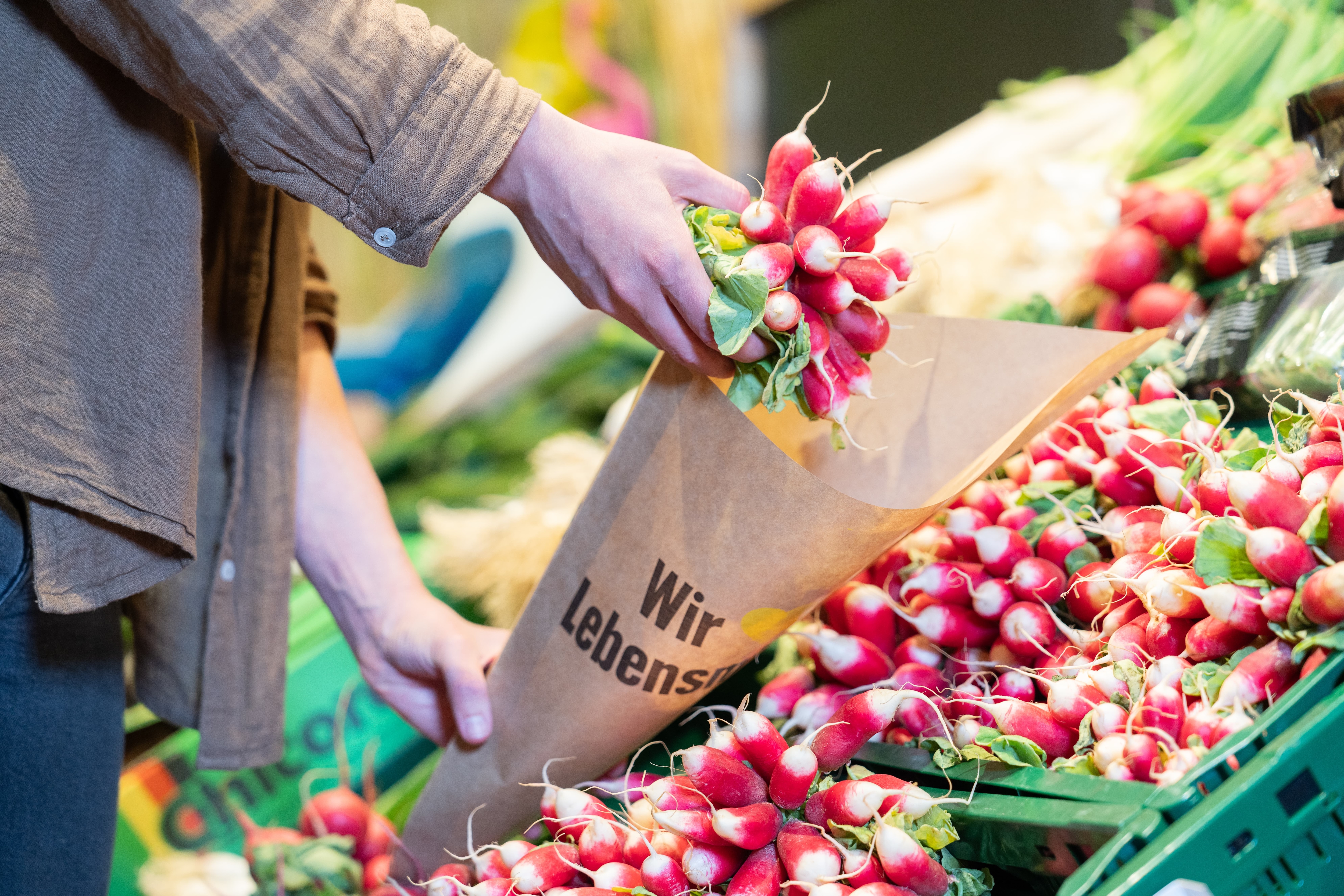 Nahaufnahme einer Person, die ein Bund Radieschen in eine Papiertüte mit der Aufschrift "Wir lieben Lebensmittel" legt.