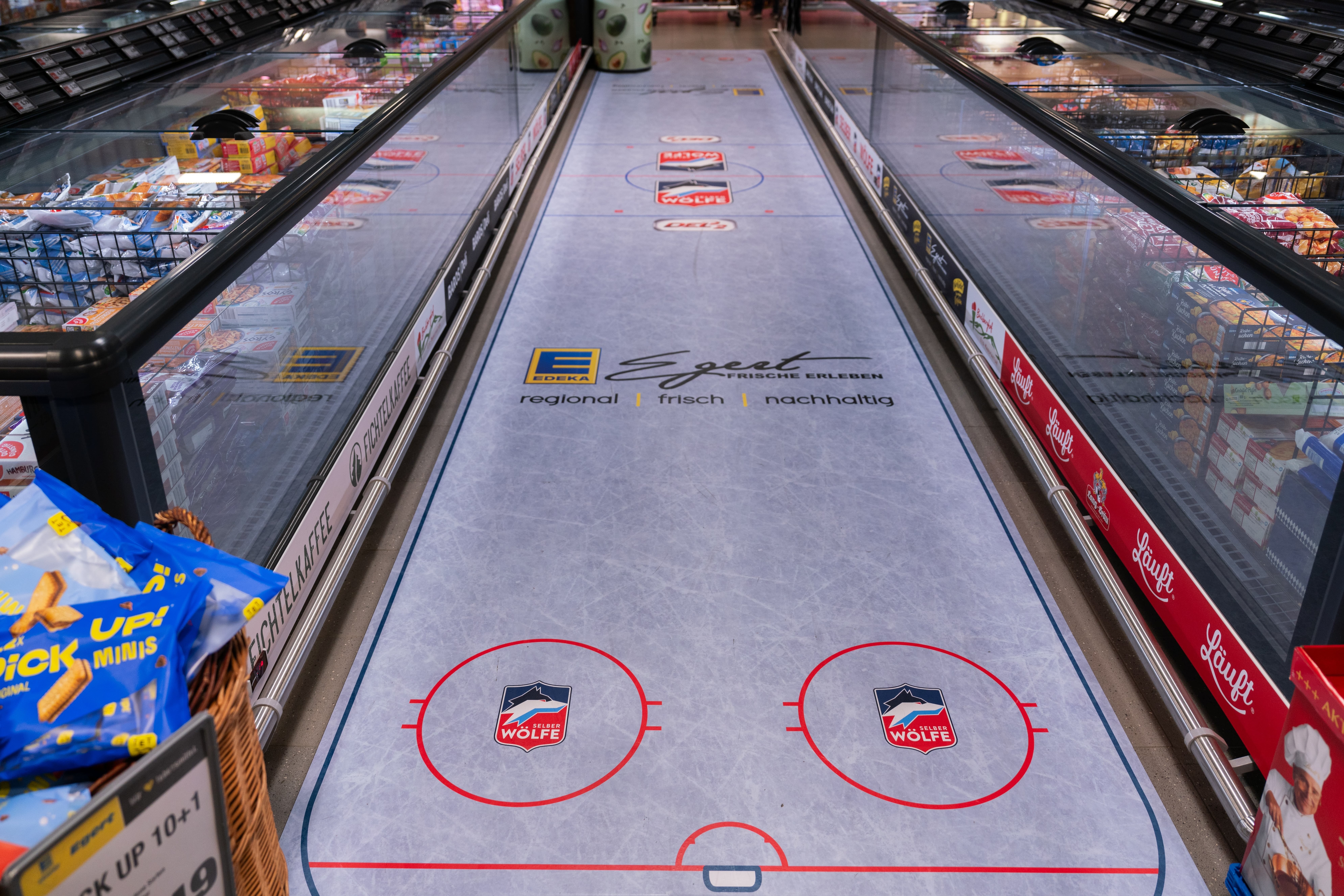 Ein Gang zwischen den Kühltruhen eines EDEKA-Marktes. Der Boden ist einer Eisfläche nachempfunden und das Logo der Selber Wölfe ist zu erkennen.