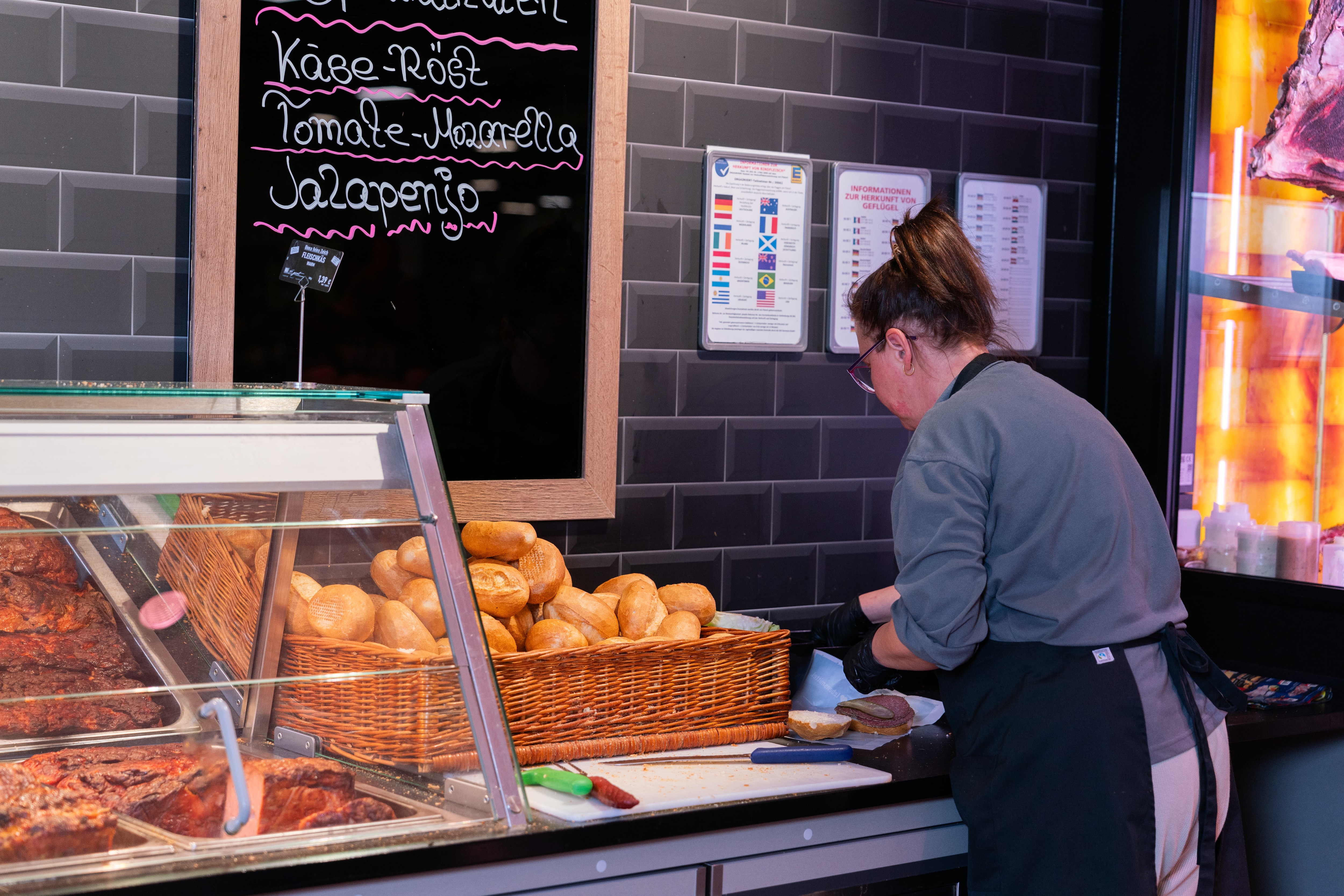 Eine Mitarbeiterin der Frischetheke belegt ein Brötchen mit Wurst und Gewürzgurke.