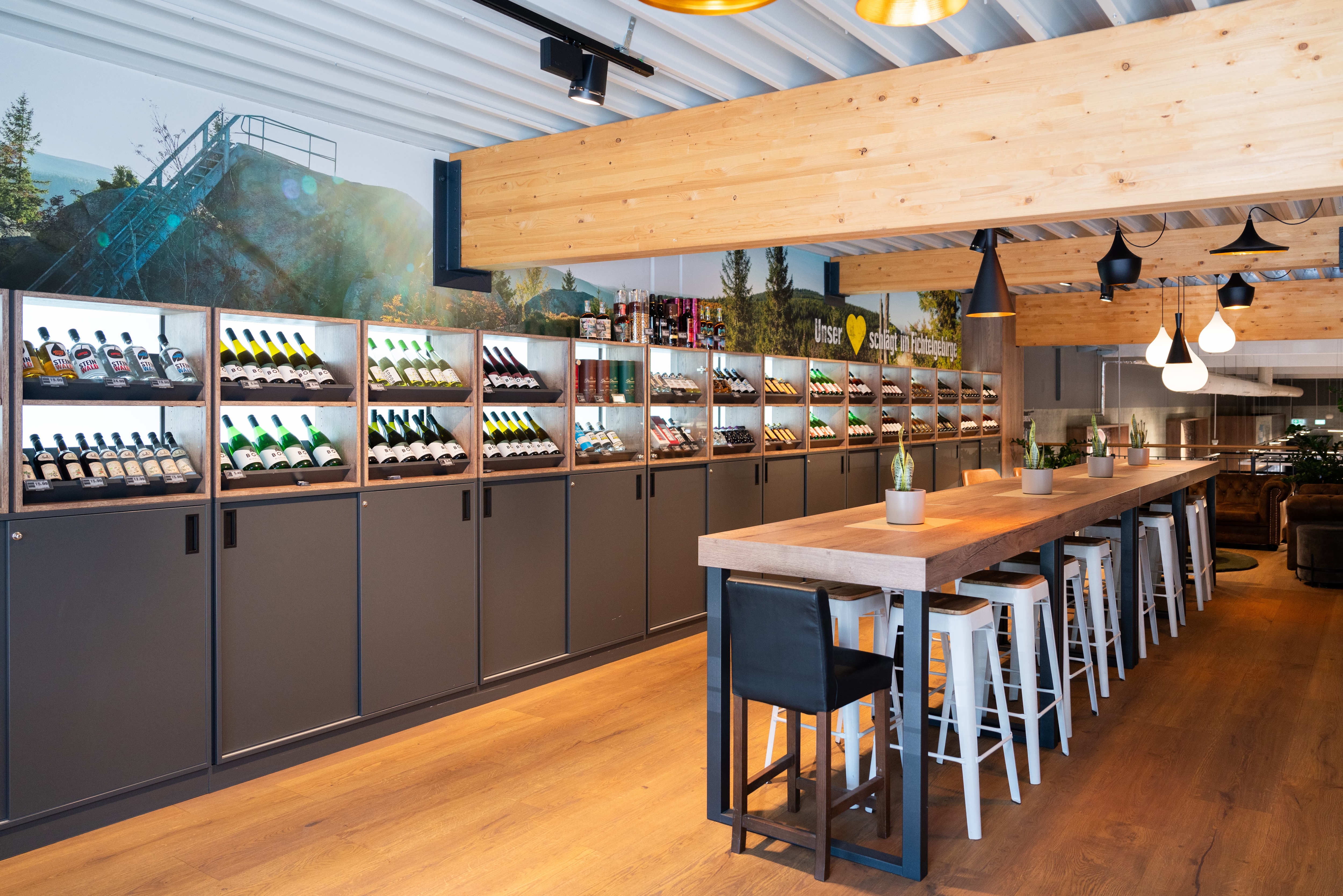 Ein Raum mit einem langen Tisch in der Mitte. An der Wand sind verschiedene Weinflaschen drapiert.