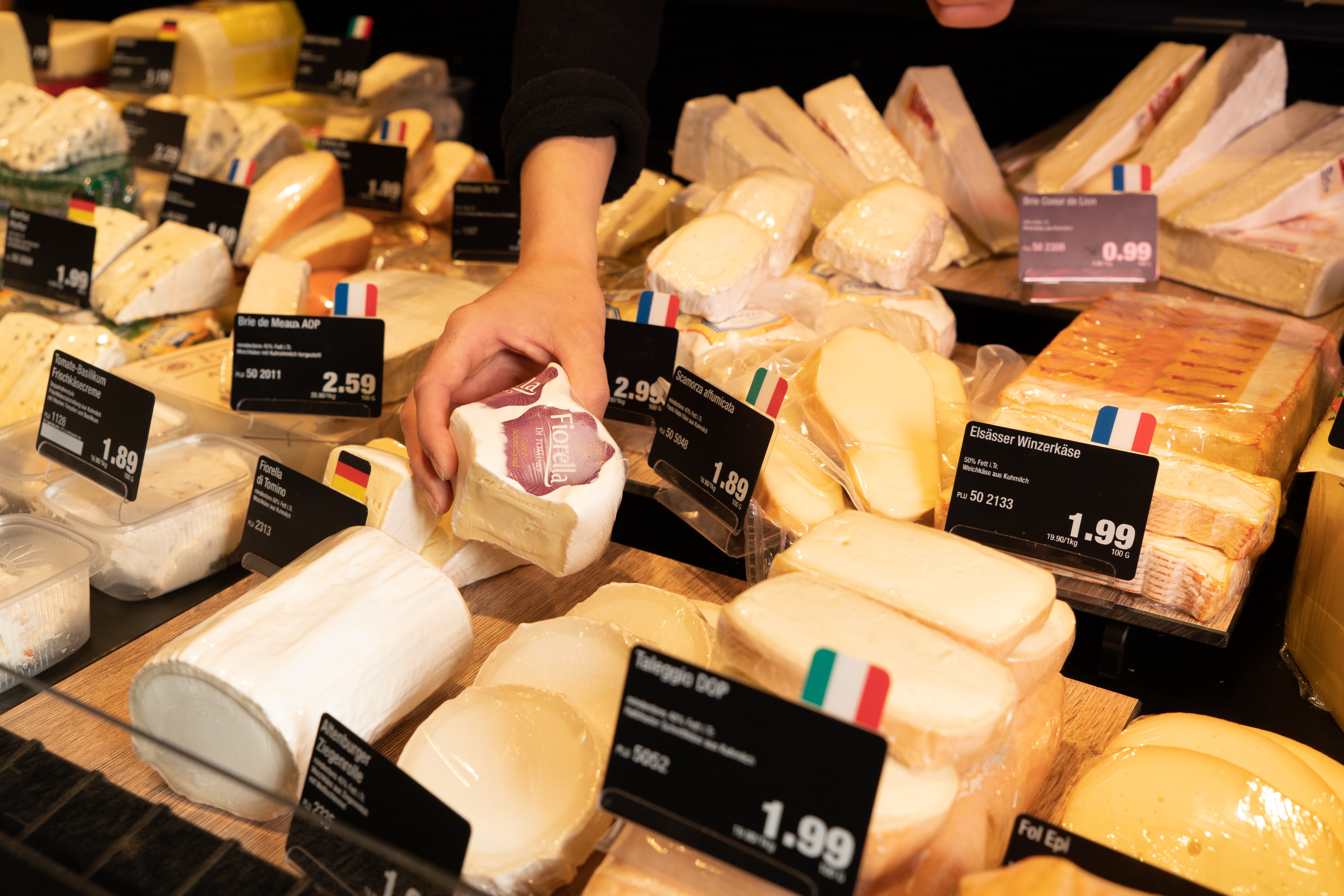 Eine Hand nimmt ein Stück Käse aus der Frischetheke eines Edeka-Marktes.