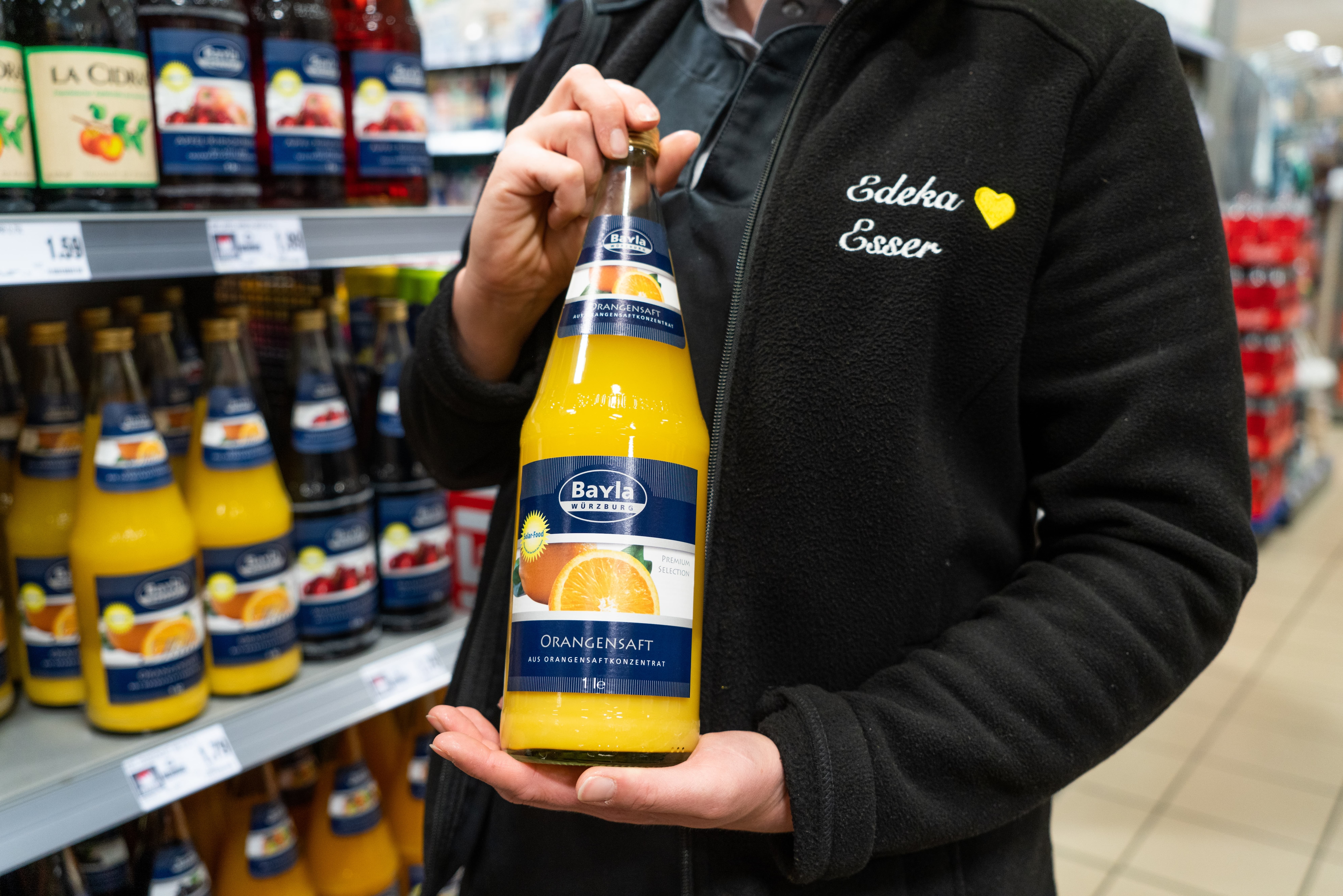 Eine Edeka-Mitarbeiterin hält eine Flasche Orangensaft in den Händen.