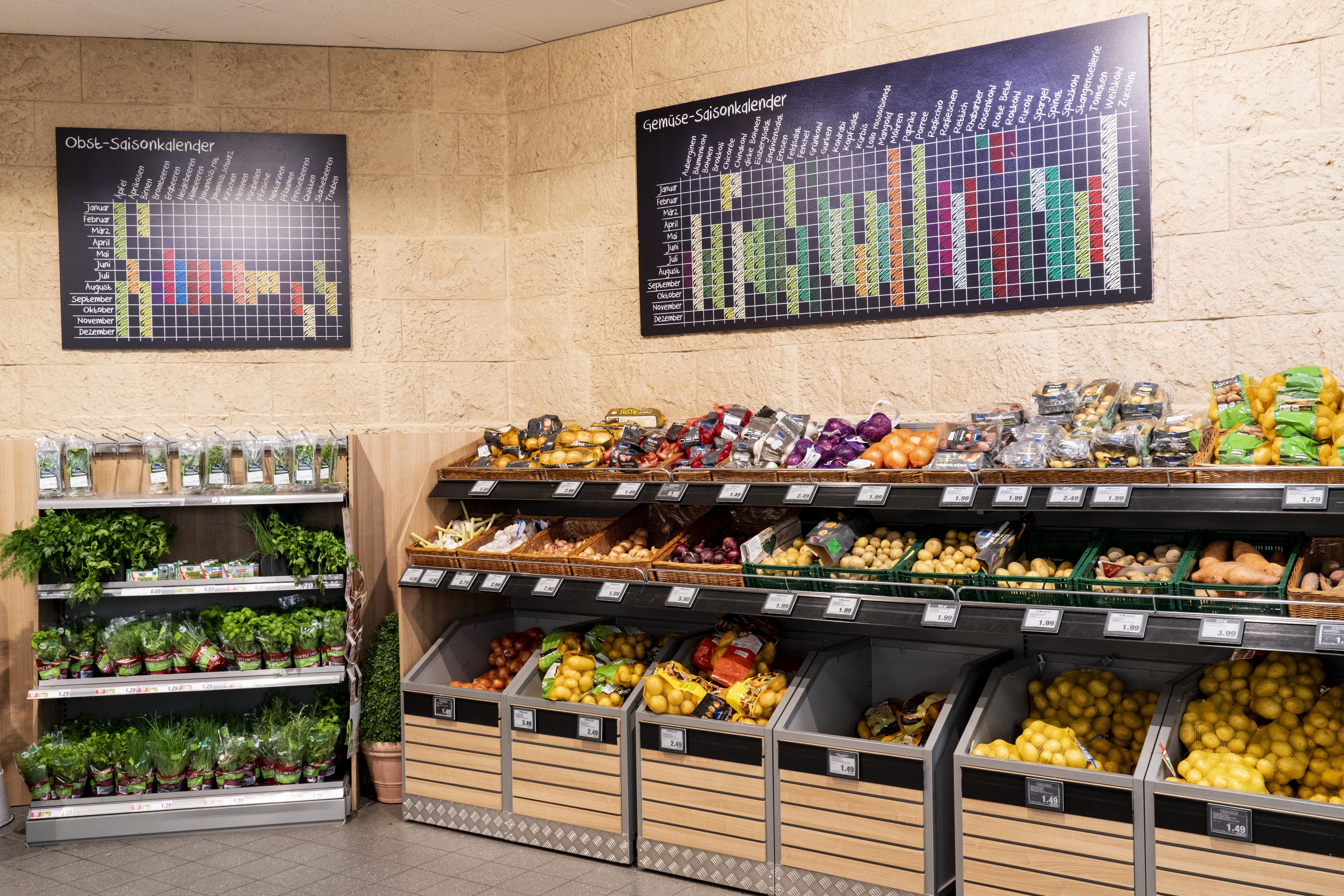 Über dem Kartoffelregal hängen bunte Saisonkalender für Gemüse und für Obst.