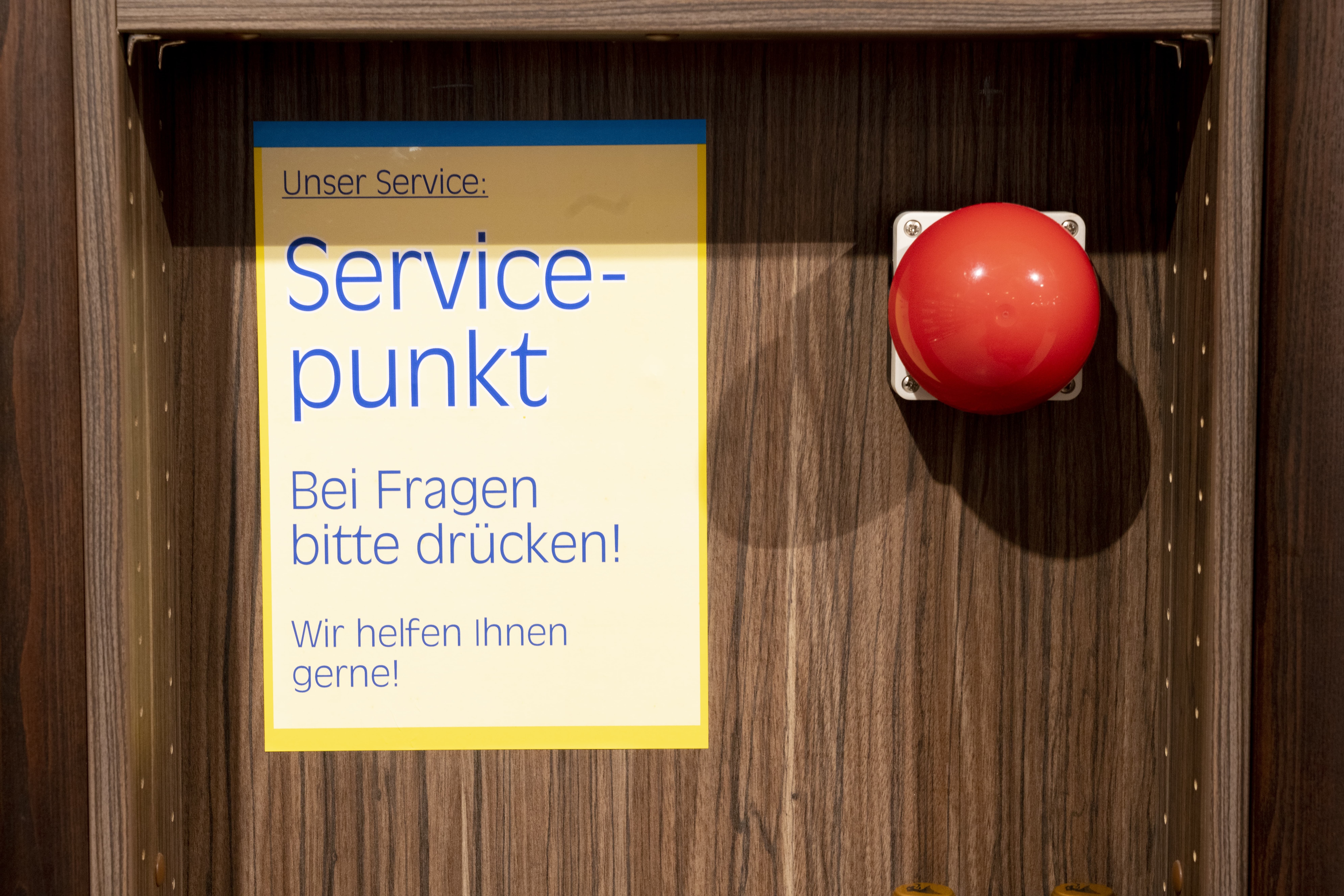 Ein roter Alarmknopf mit Schild: Unser Service: Servicepunkt. Bei Fragen bitte drücken! Wir helfen Ihnen gerne!
