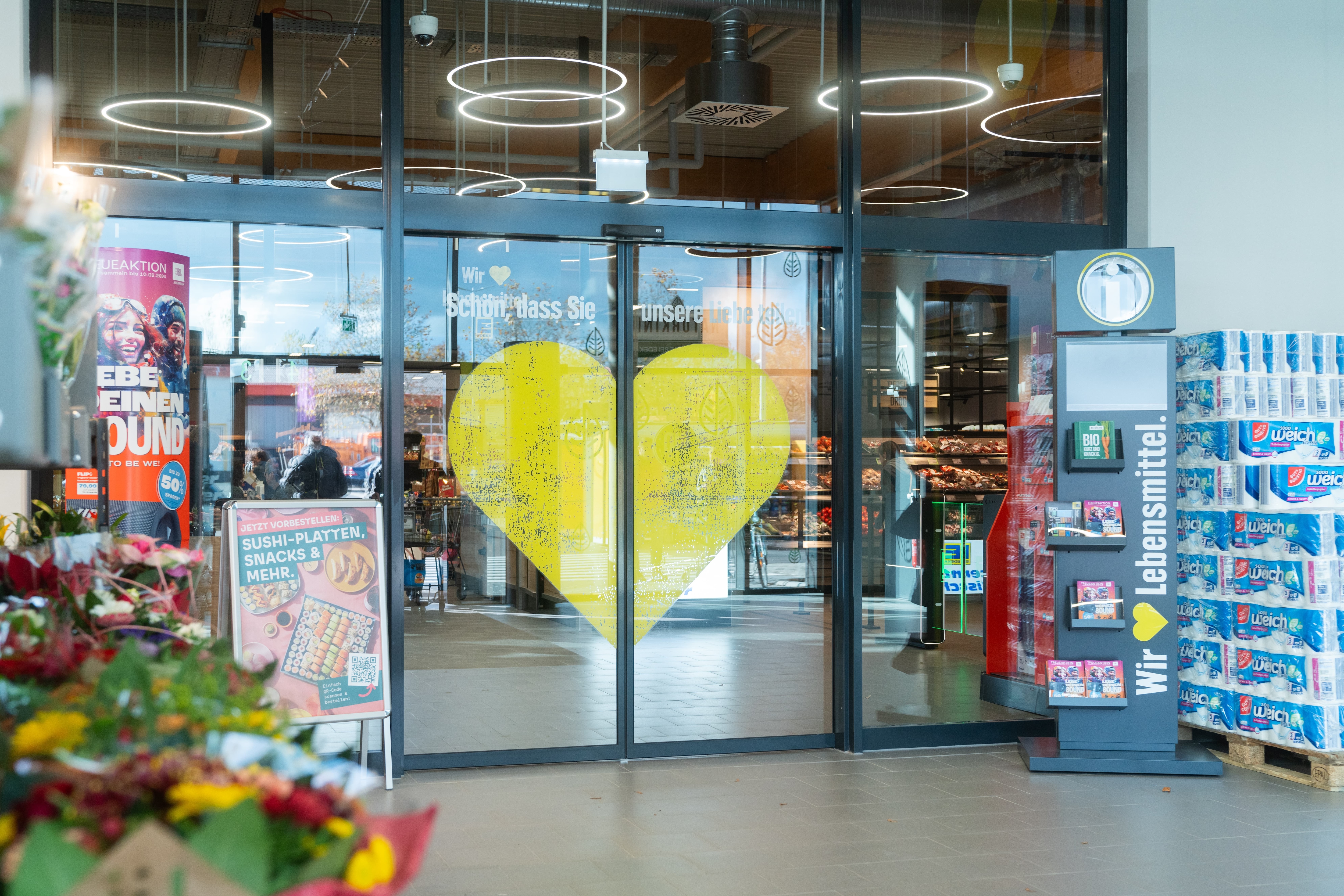 Eine gläserne Automatiktür mit einem gelben Herzen. Darüber steht: Schön, dass Sie unsere Liebe teilen.