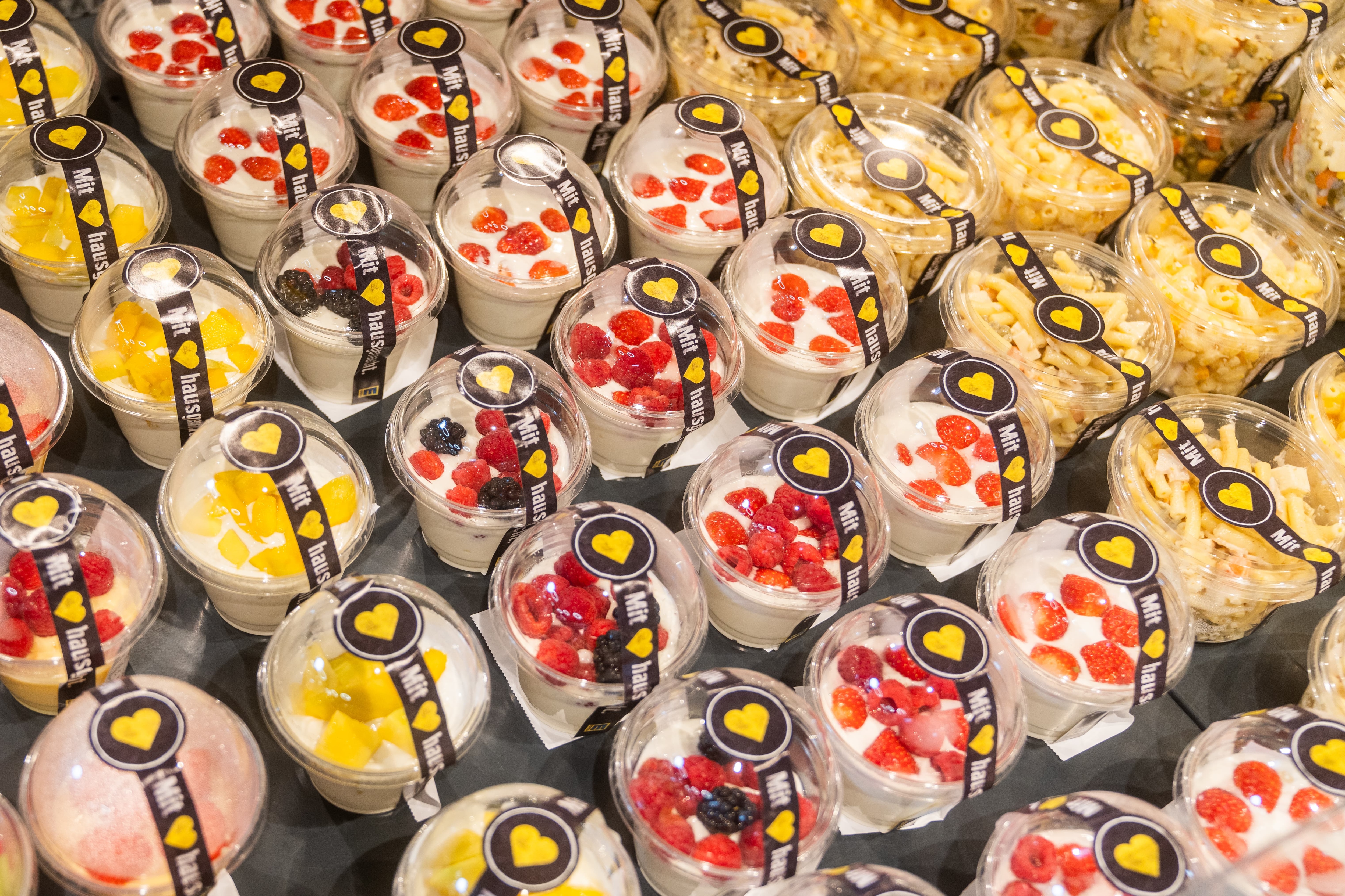 Etwa 20 transparente Plastik-Behälter mit Joghurt sowie mit Nudeln.