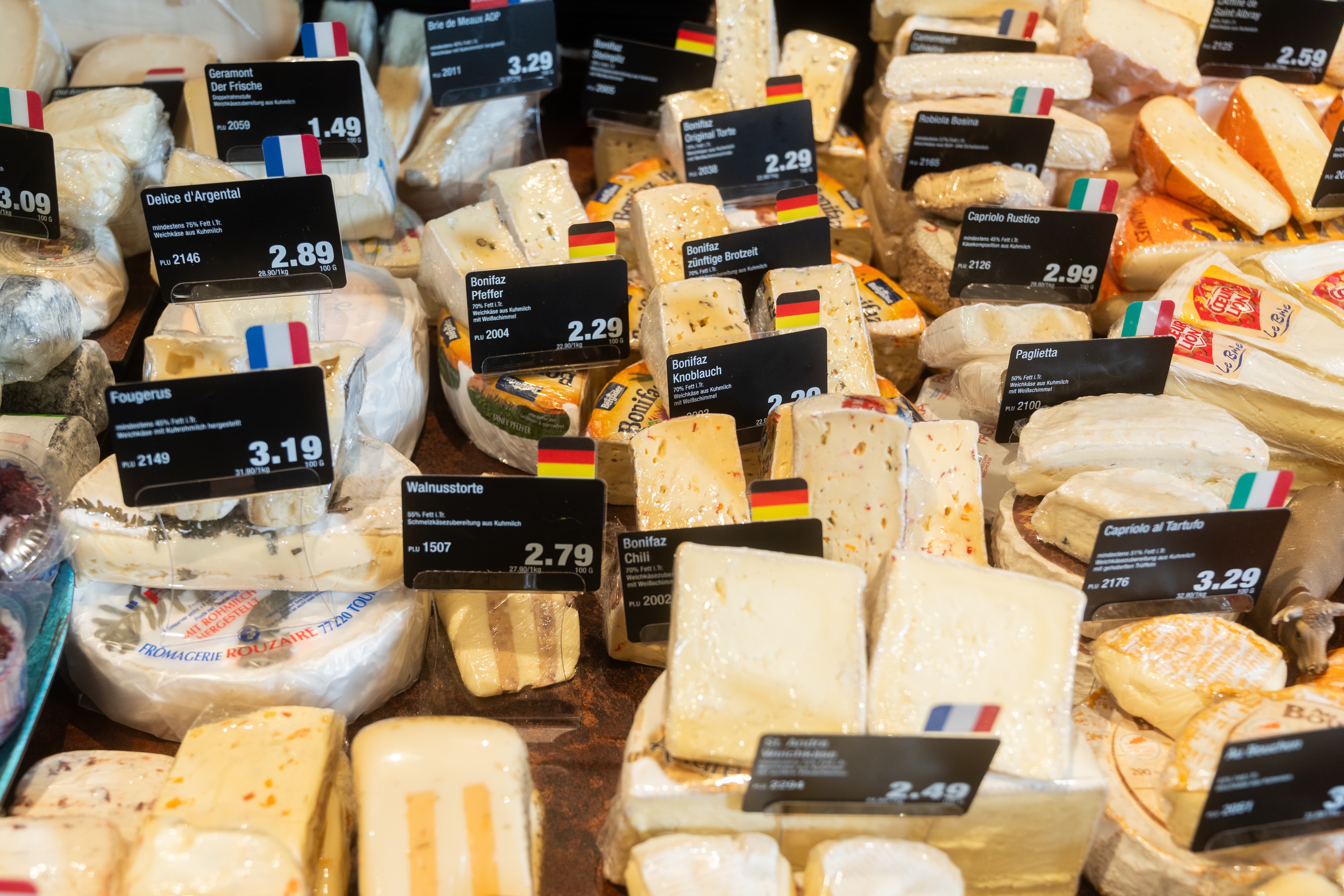Verschiedene Käsesorten mit Preisschildern in einer Auslage.