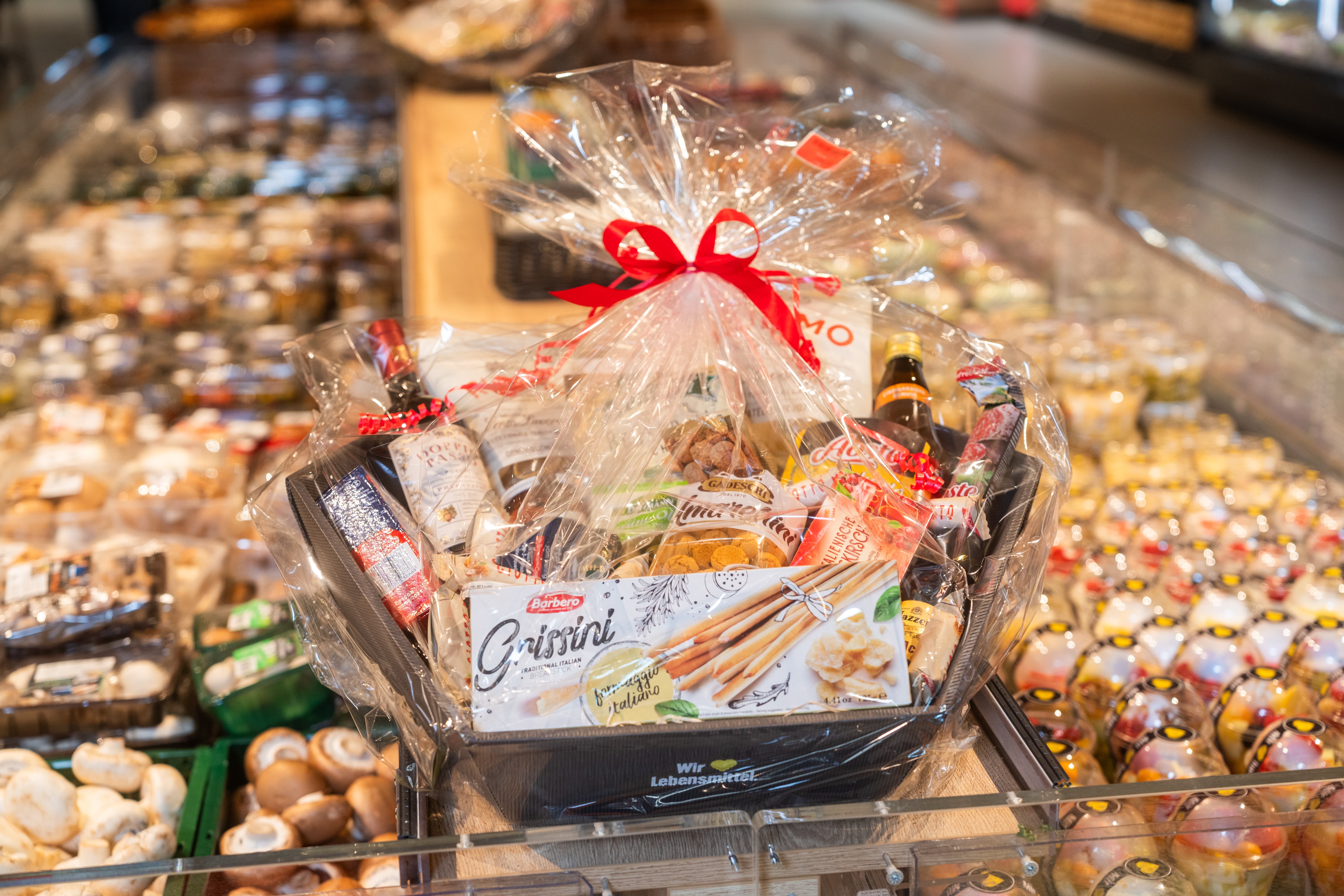 Ein mit Klarsichtfolie verzierter Präsentkorb mit Lebensmitteln.
