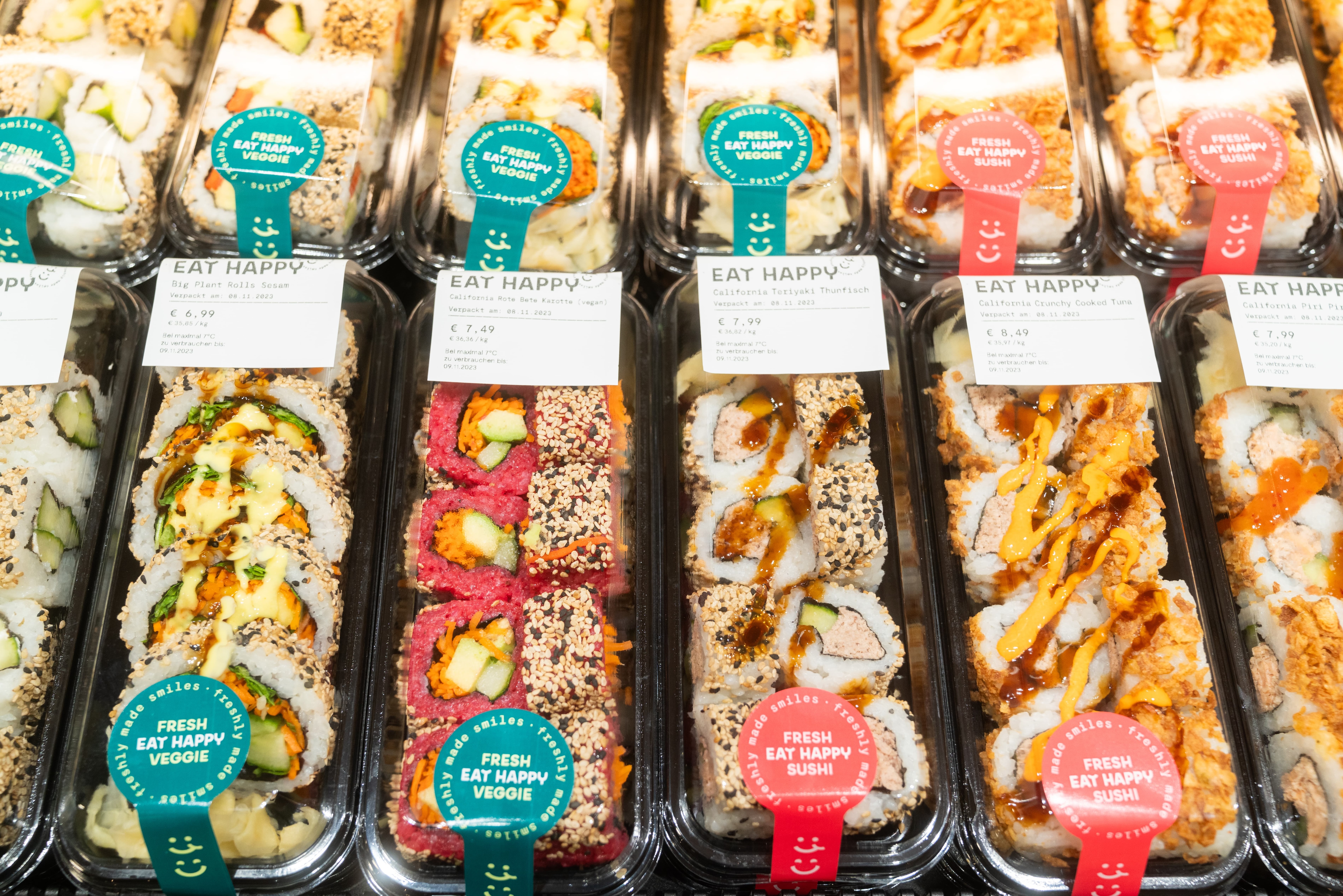 Eine Reihe von Sushipackungen von Eat Happy mit Preisschildern.