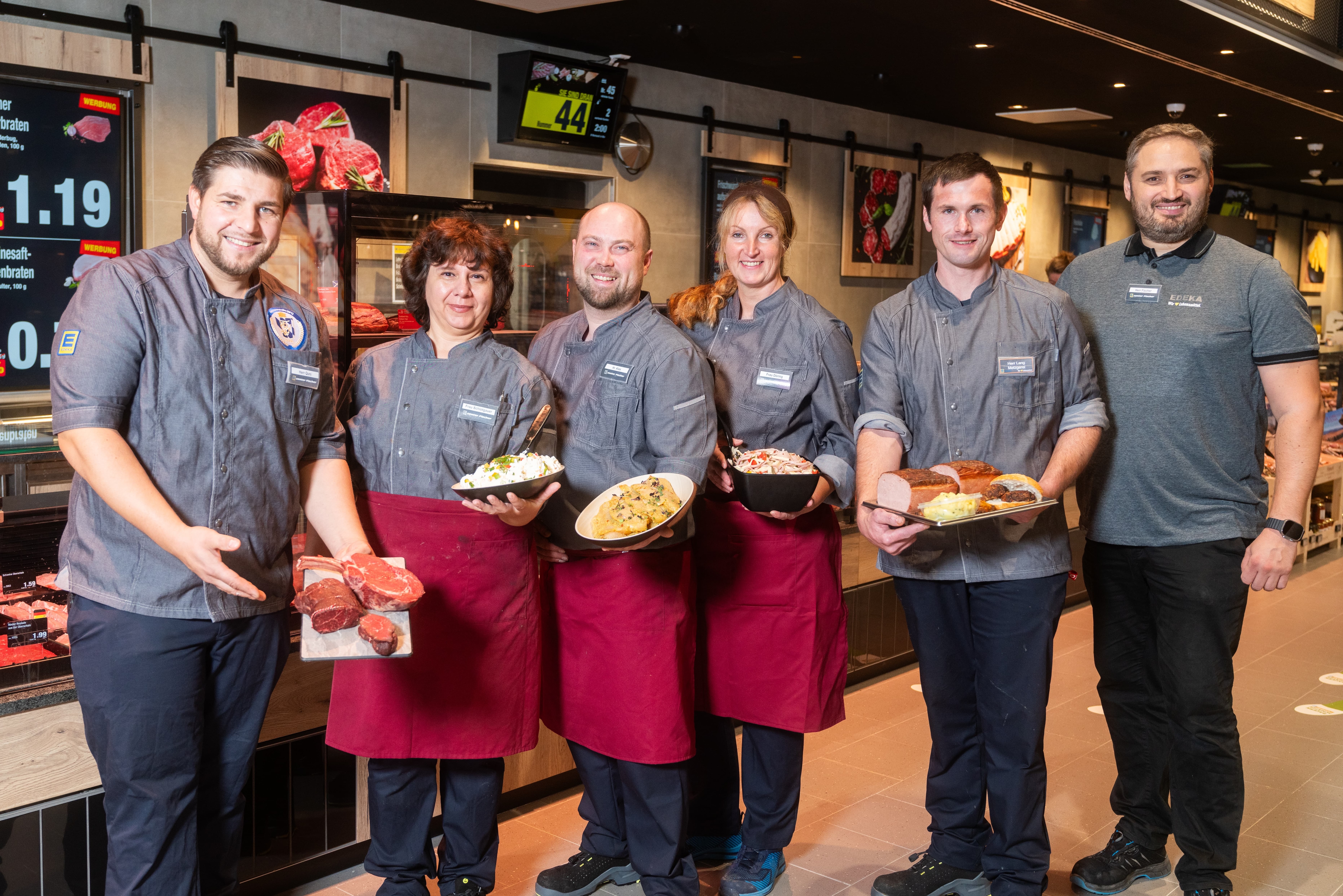 Zwei Frauen und vier Männer stehen vor der Frischetheke und präsentieren Produkte.