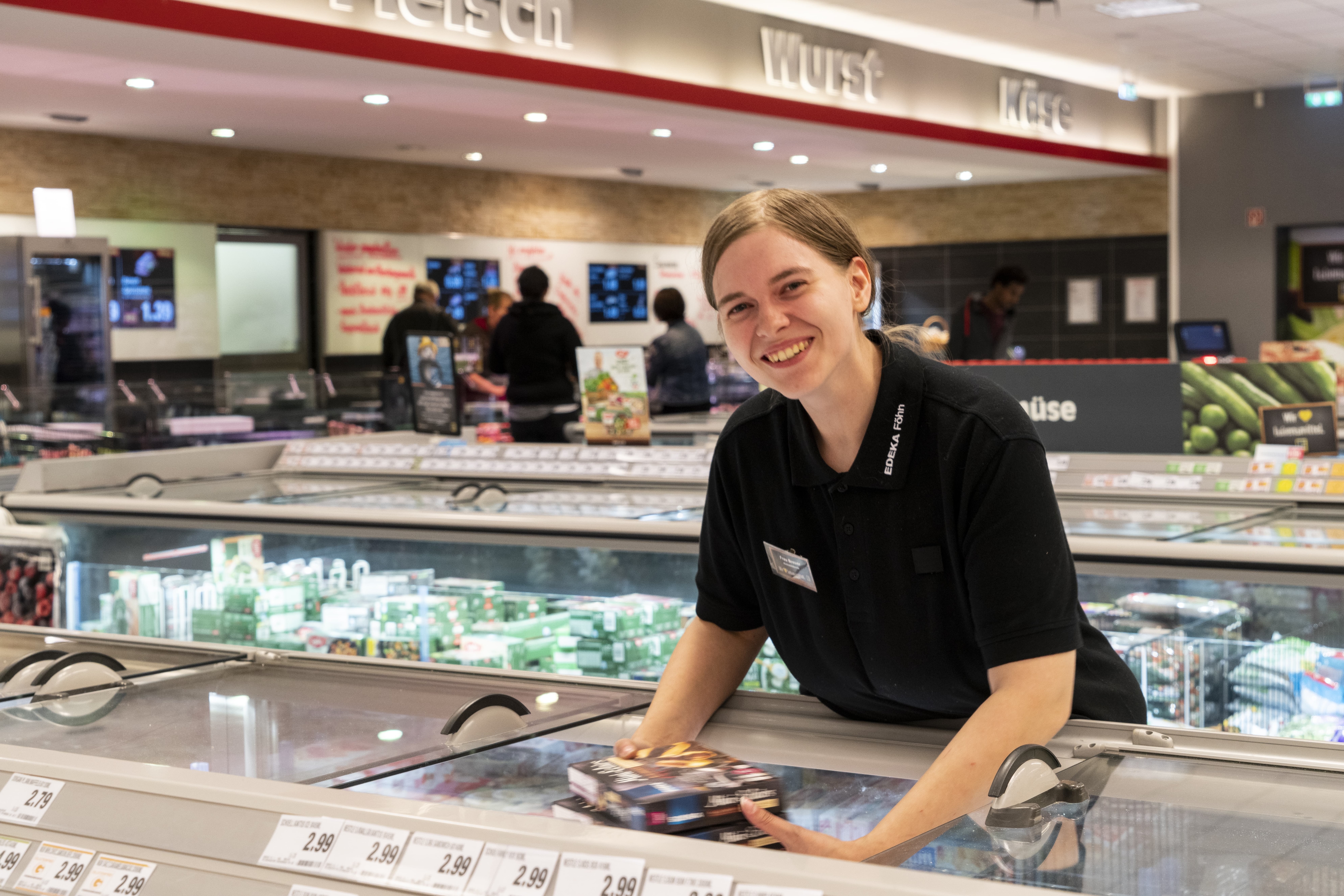 Eine junge Frau legt Produkte in die Tiefkühltruhe eines EDEKA-Markts und lächelt dabei in die Kamera.