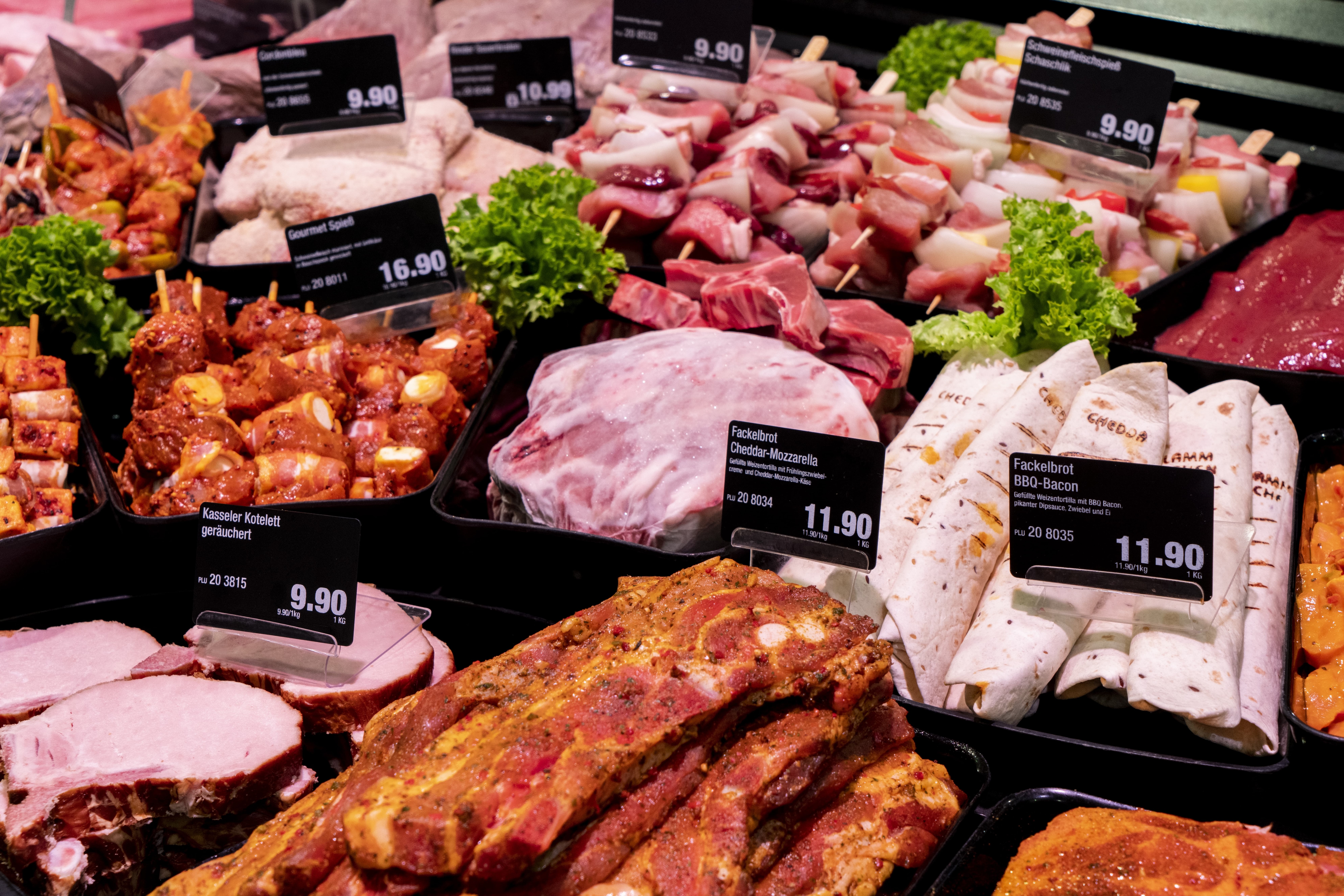 Die Fleischauslage eines EDEKA-Markts, mit Salat als Deko und Preisschildern.