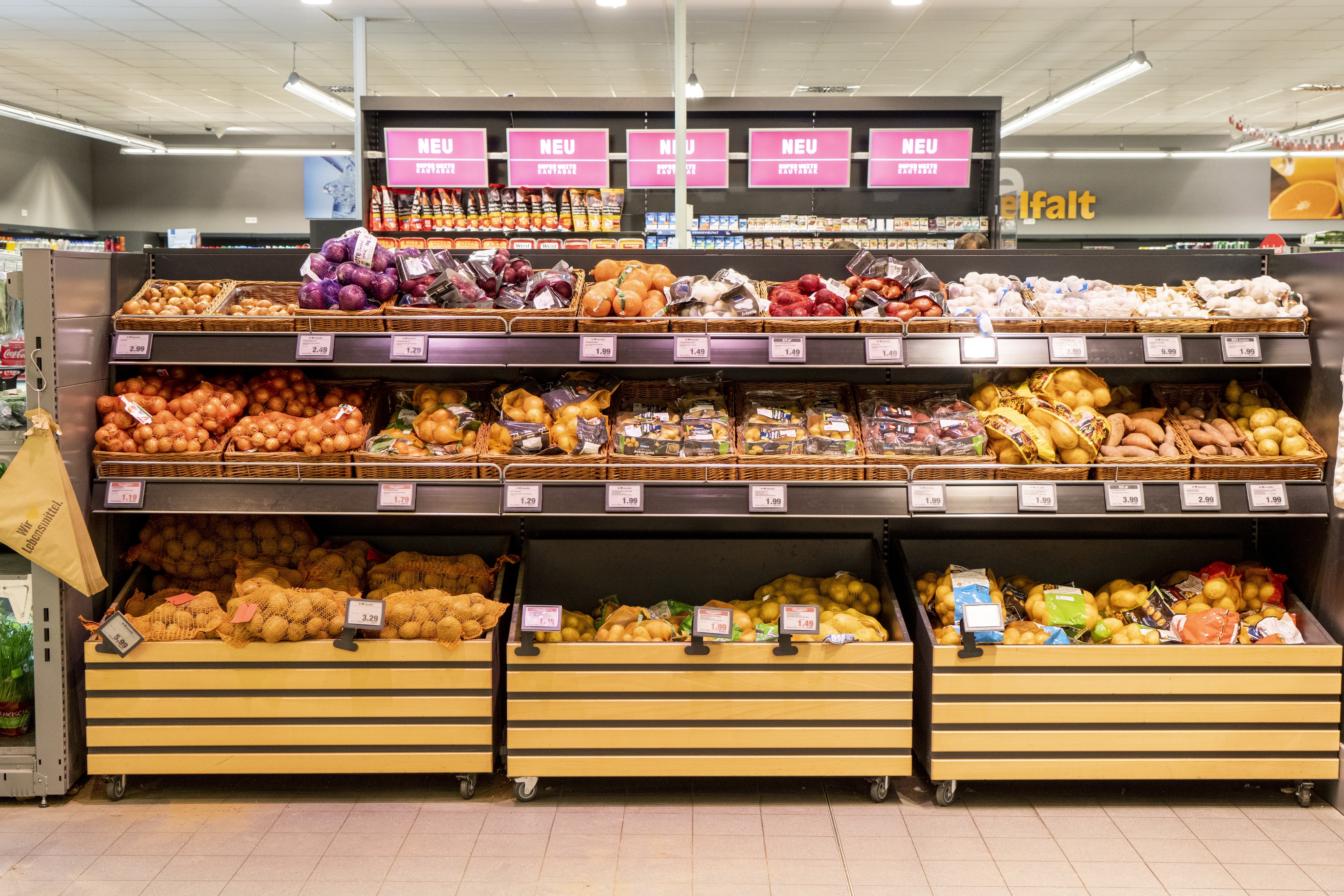 Ein Regal mit Kartoffeln, Zwiebeln, Knoblauch und Süßkartoffeln in der Gemüseabteilung eines EDEKA-Markts.