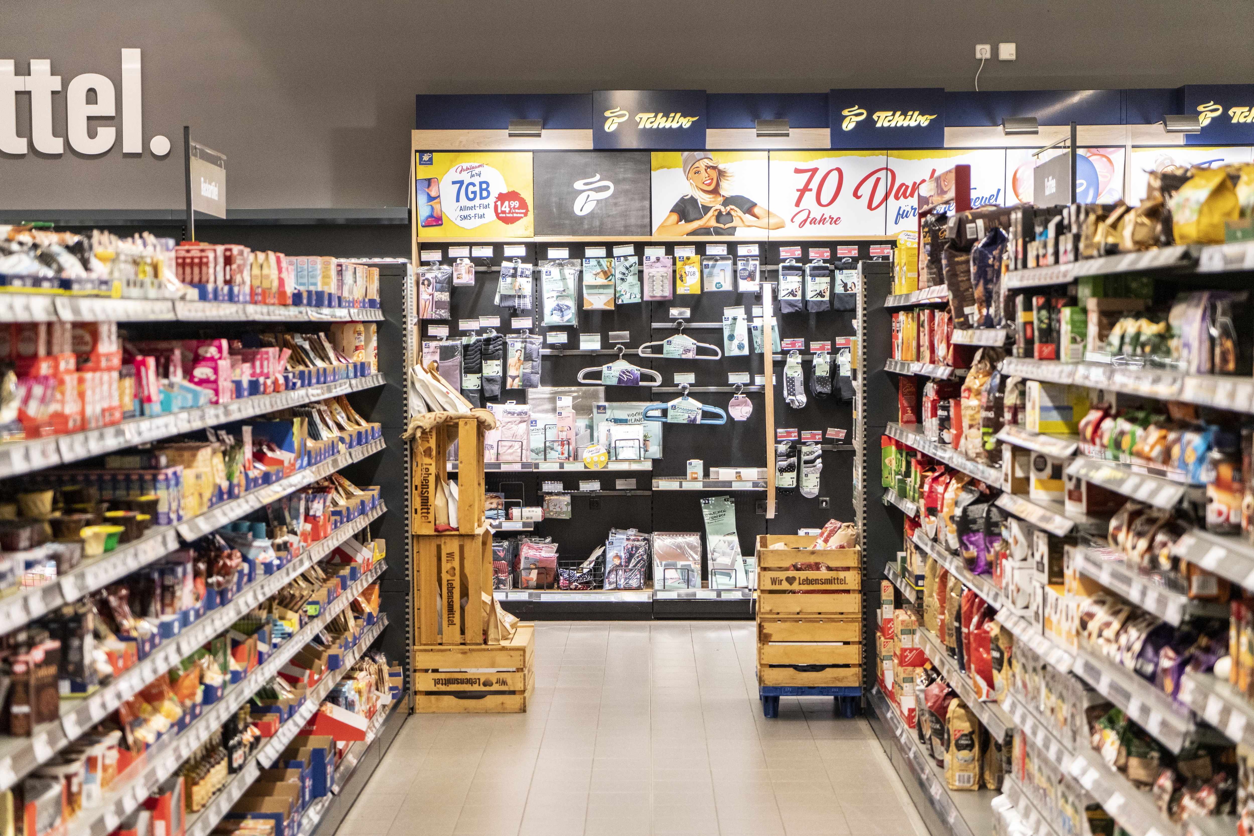 Die Tchiboabteilung eines EDEKA-Markts, gesehen aus einem Gang zwischen zwei Regalen.