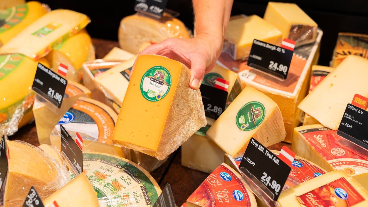 Eine Hand legt ein Stück Käse in die Auslage einer Käsetheke.