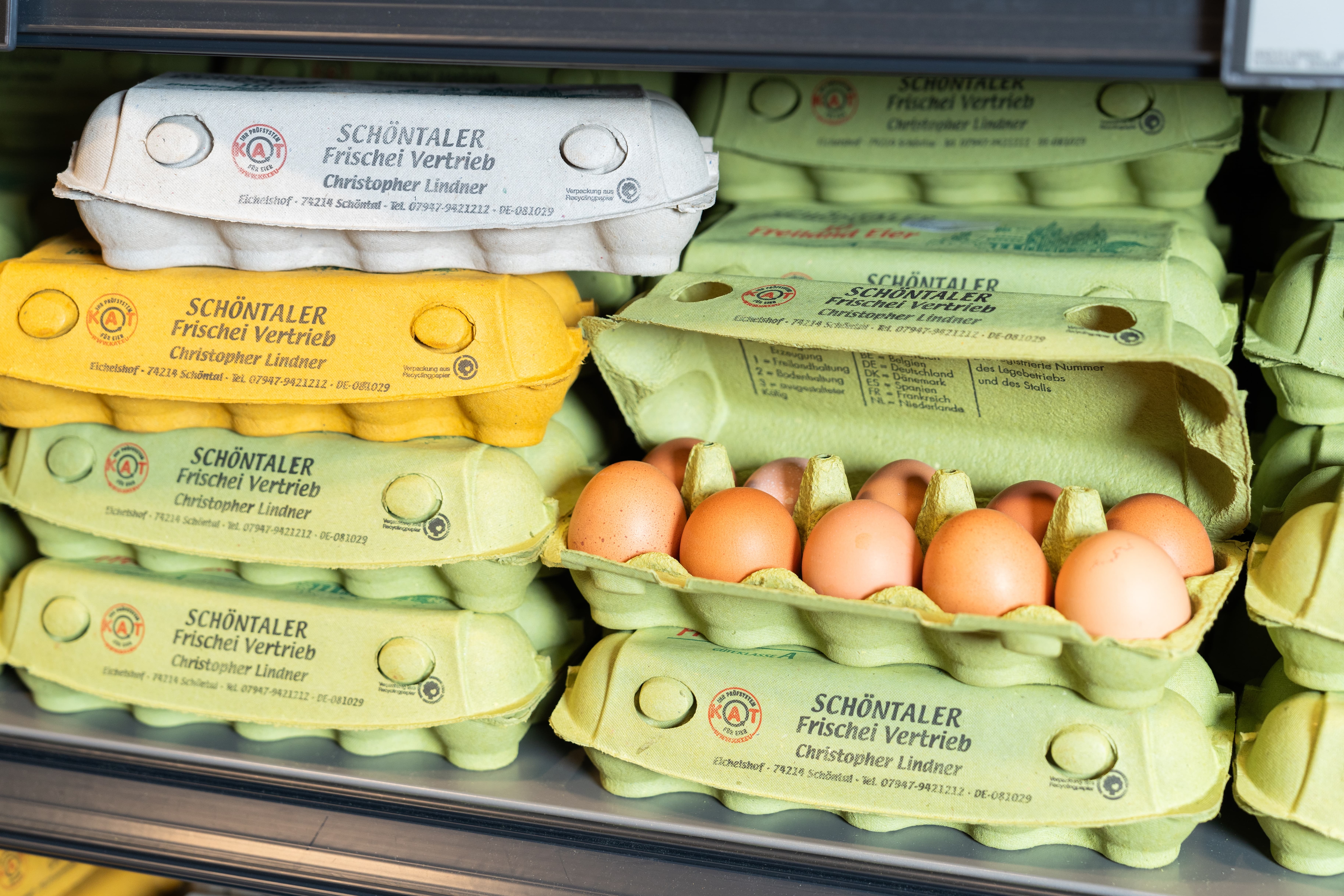 Nahaufnahme aufeinandergestapelter Eierkartons in einem Regal, ein Eierkarton ist geöffnet.