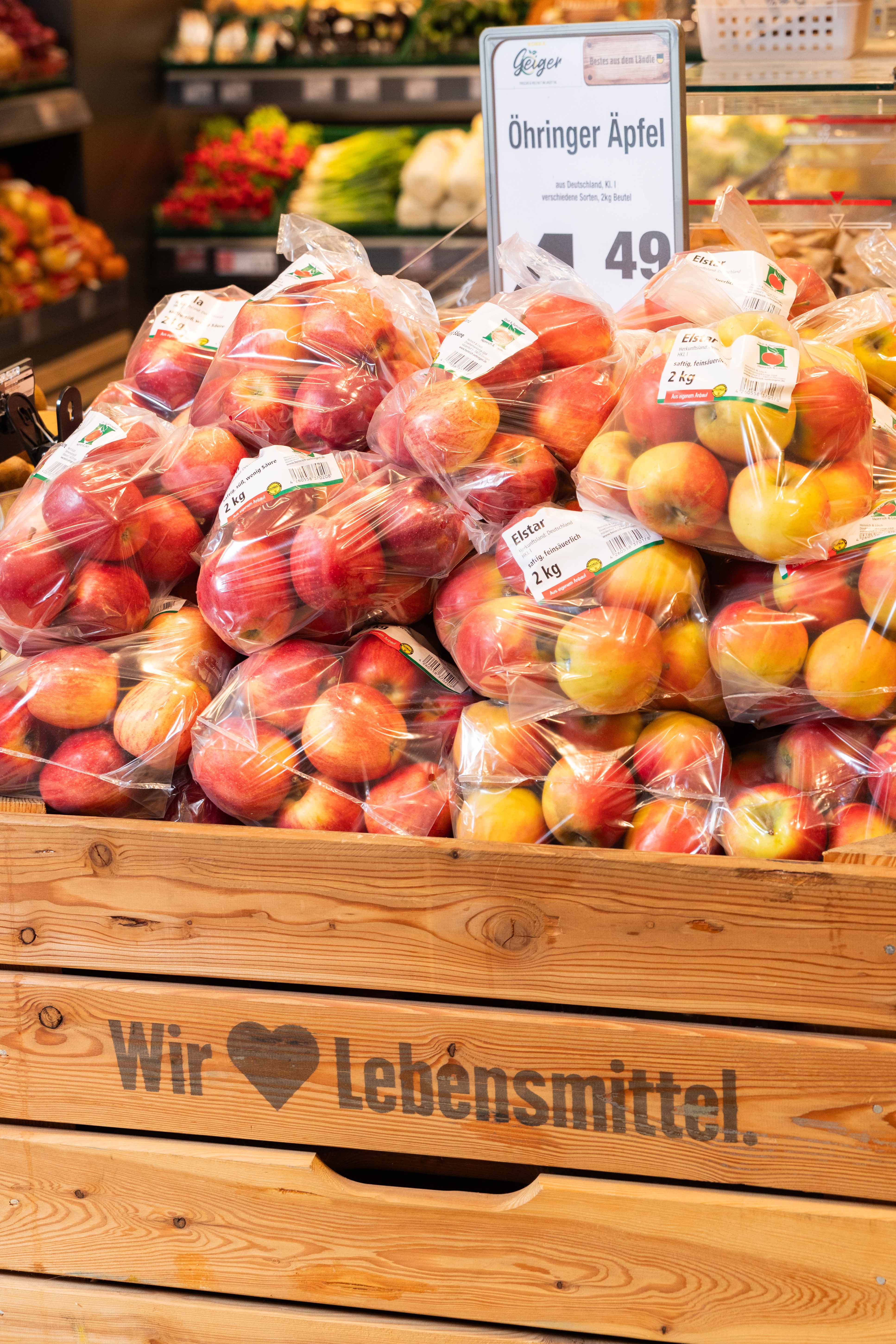 Mehrere Äpfel in Plastikbeuteln in einer Holzkiste, auf einem Schild steht "Öhringer Äpfel"