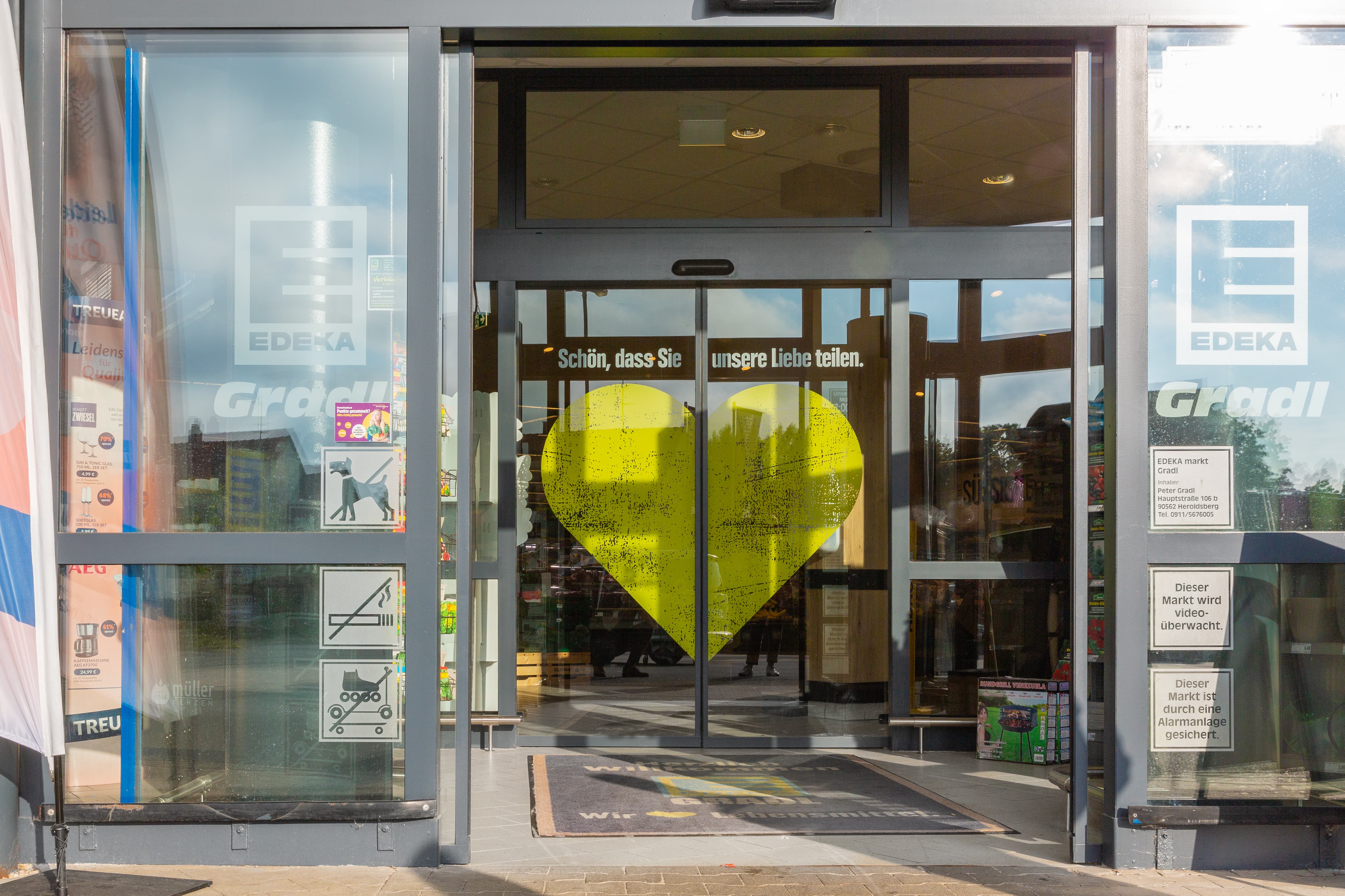 Die Eingangstür eines Edeka-Marktes bedruckt mit einem großen gelben Herz.