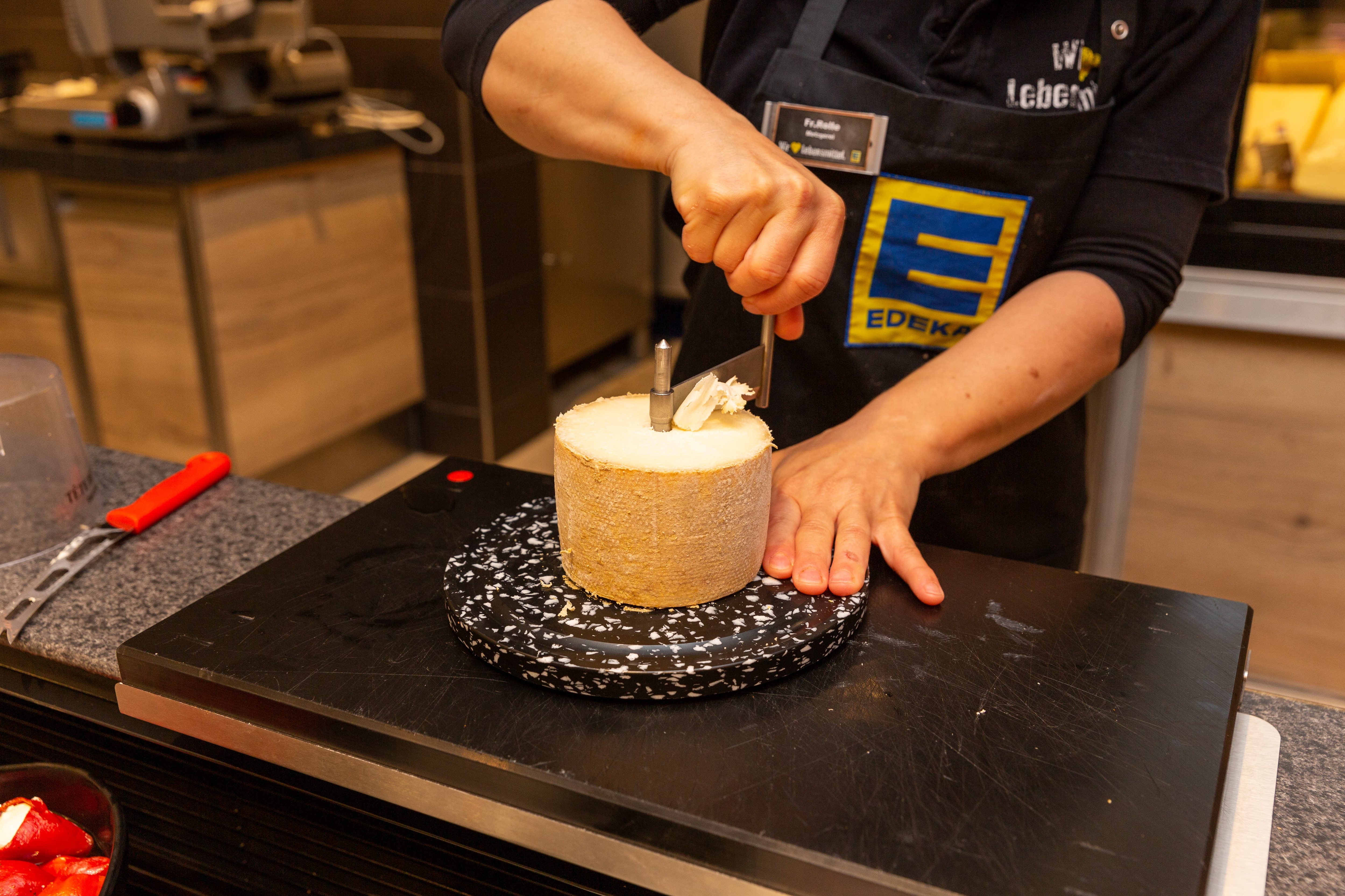 Eine Mitarbeiterin der Frischetheke hobelt Käse.