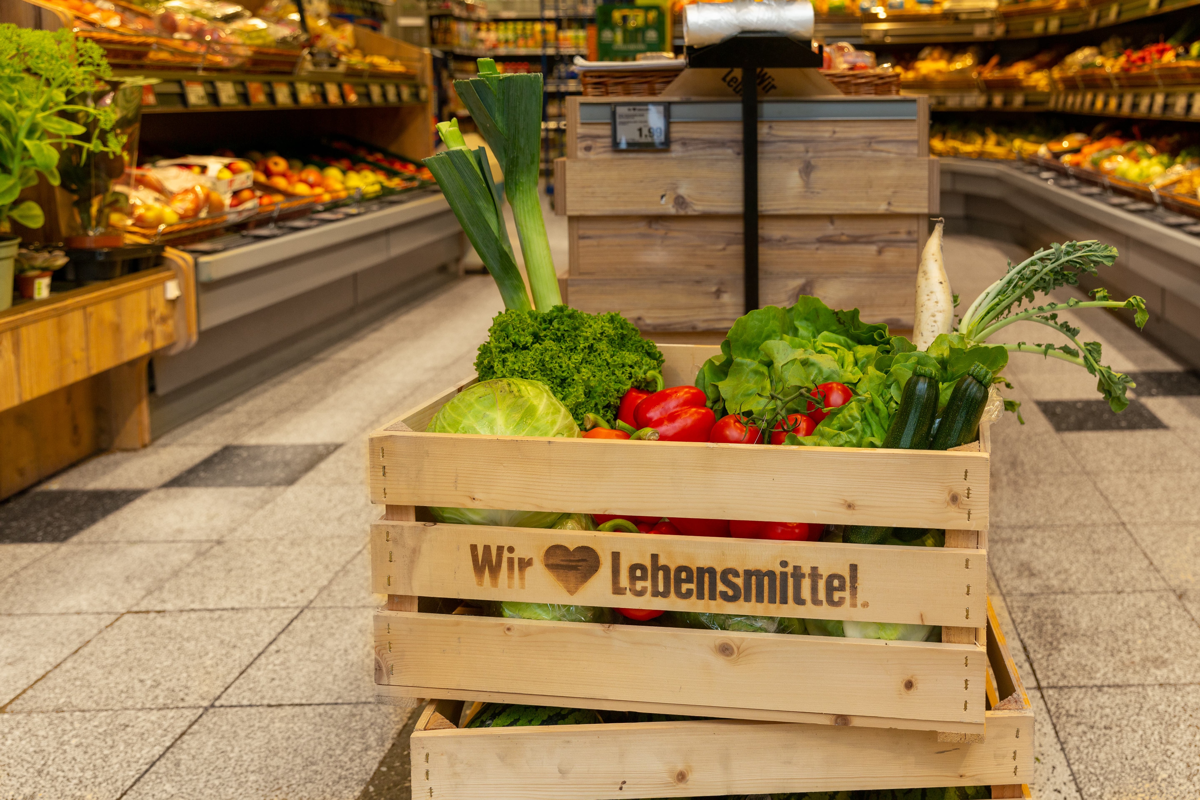 Eine Holzkiste gefüllt mit verschiedenen Gemüsesorten in der Obst- und Gemüseabteilung eines Edeka-Marktes.