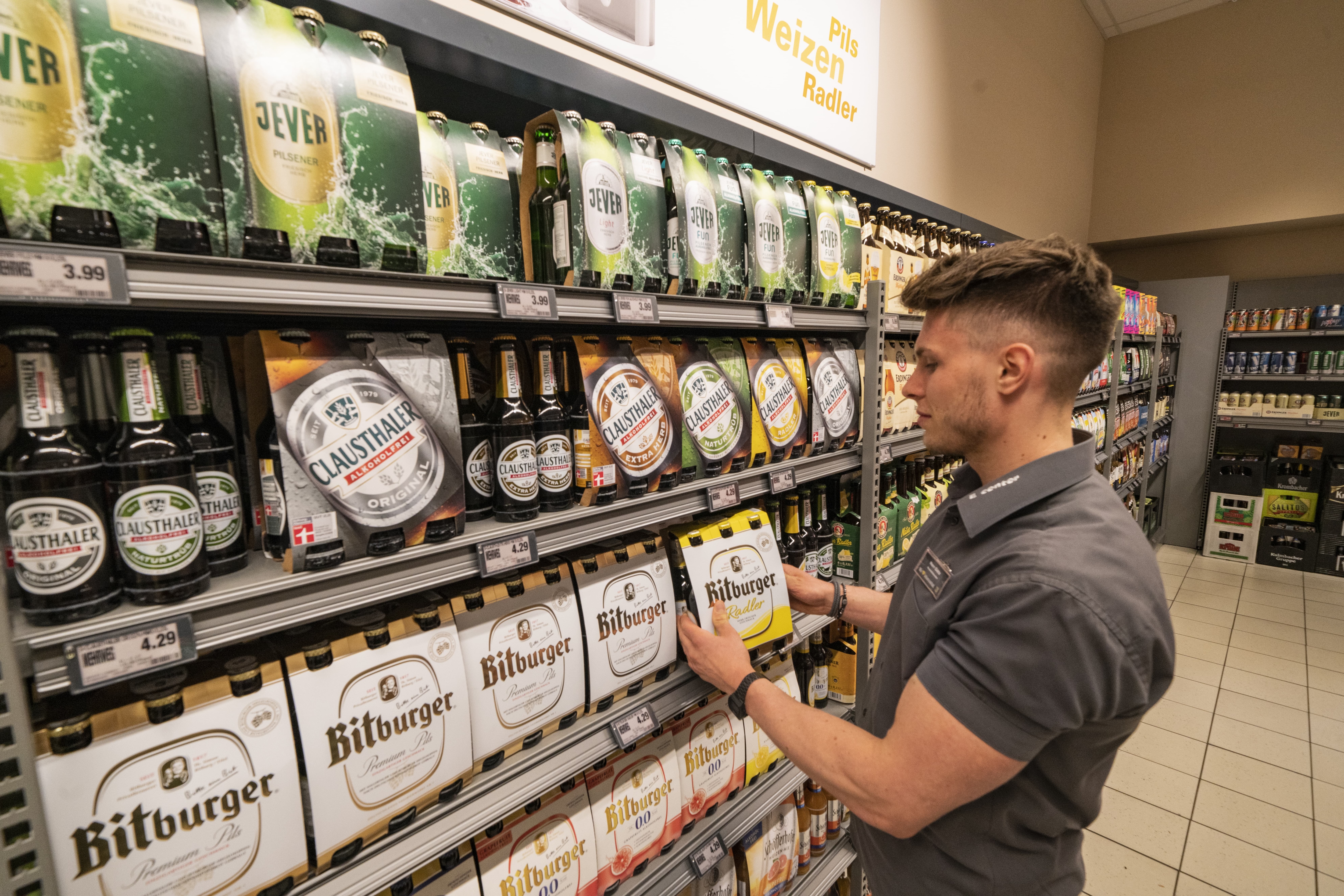 In der Getränkeabteilung eines EDEKA-Markts stellt ein junger Mitarbeiter einen Sixer Bier ins Regal.