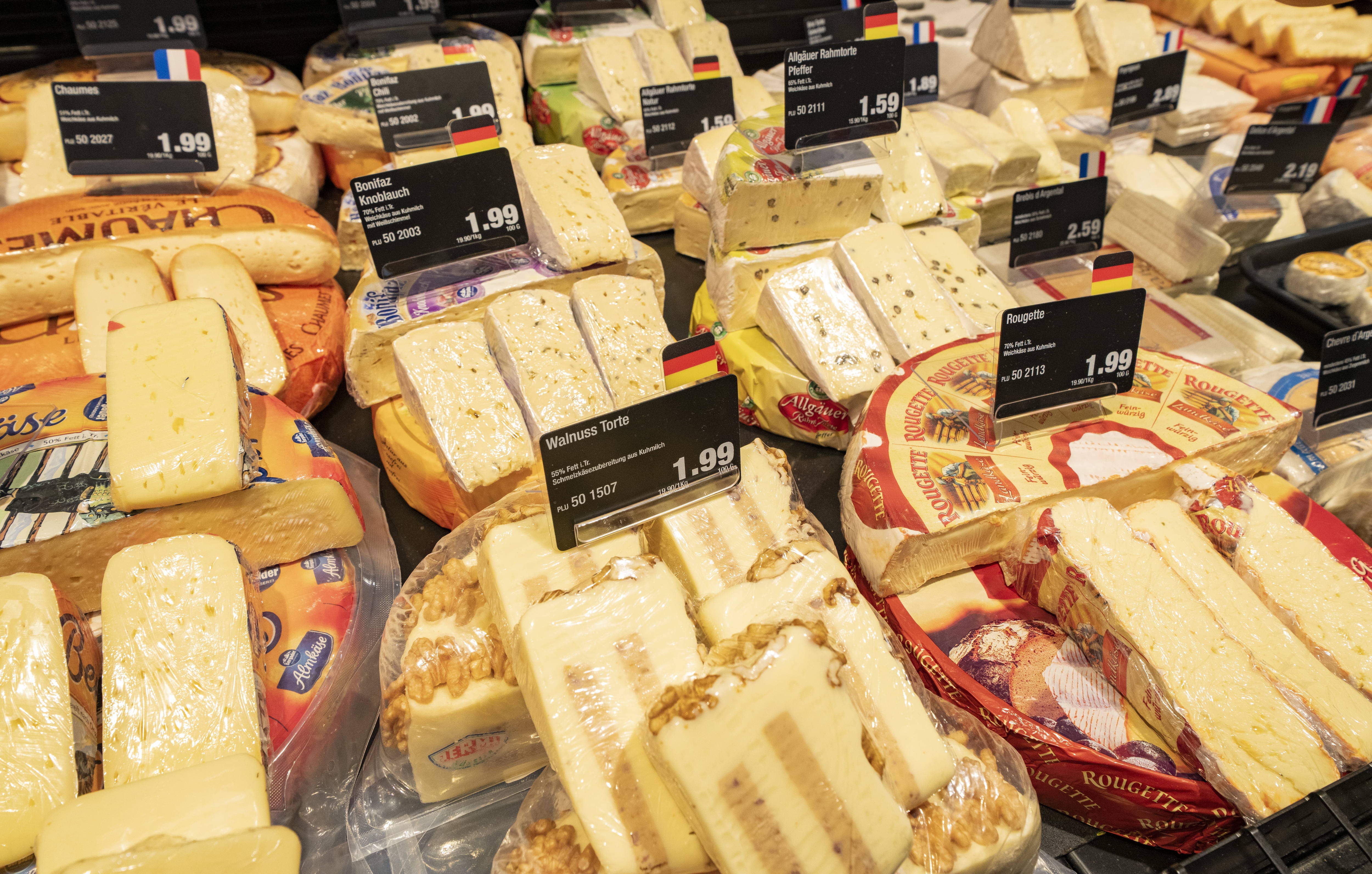 Käseauslage einer Bedienungstheke mit vielen verschiedenen Käsesorten und Preisschildern.