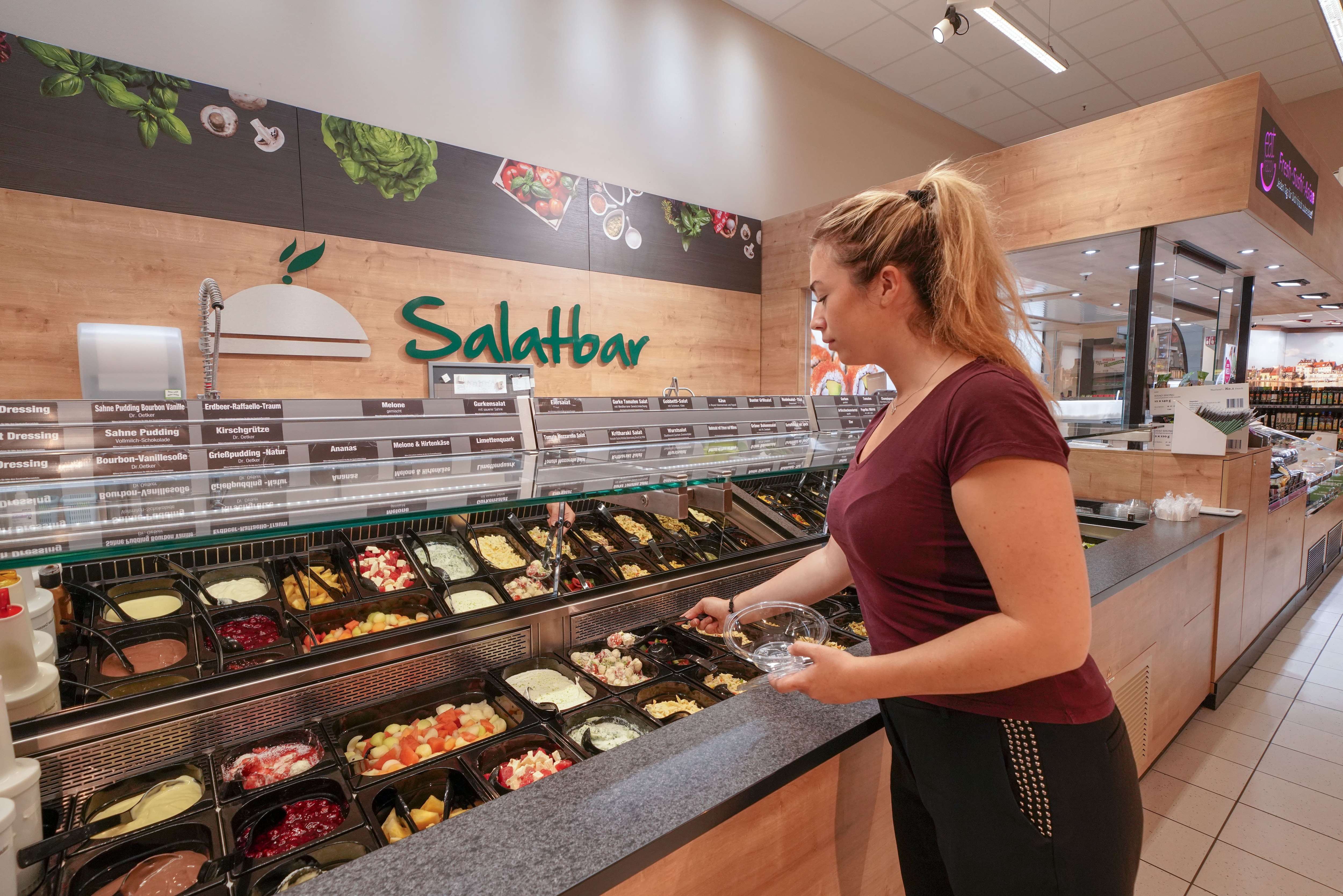 An der großzügigen Salatbar eines EDEKA-Markts nimmt sich eine Kundin etwas Salat.