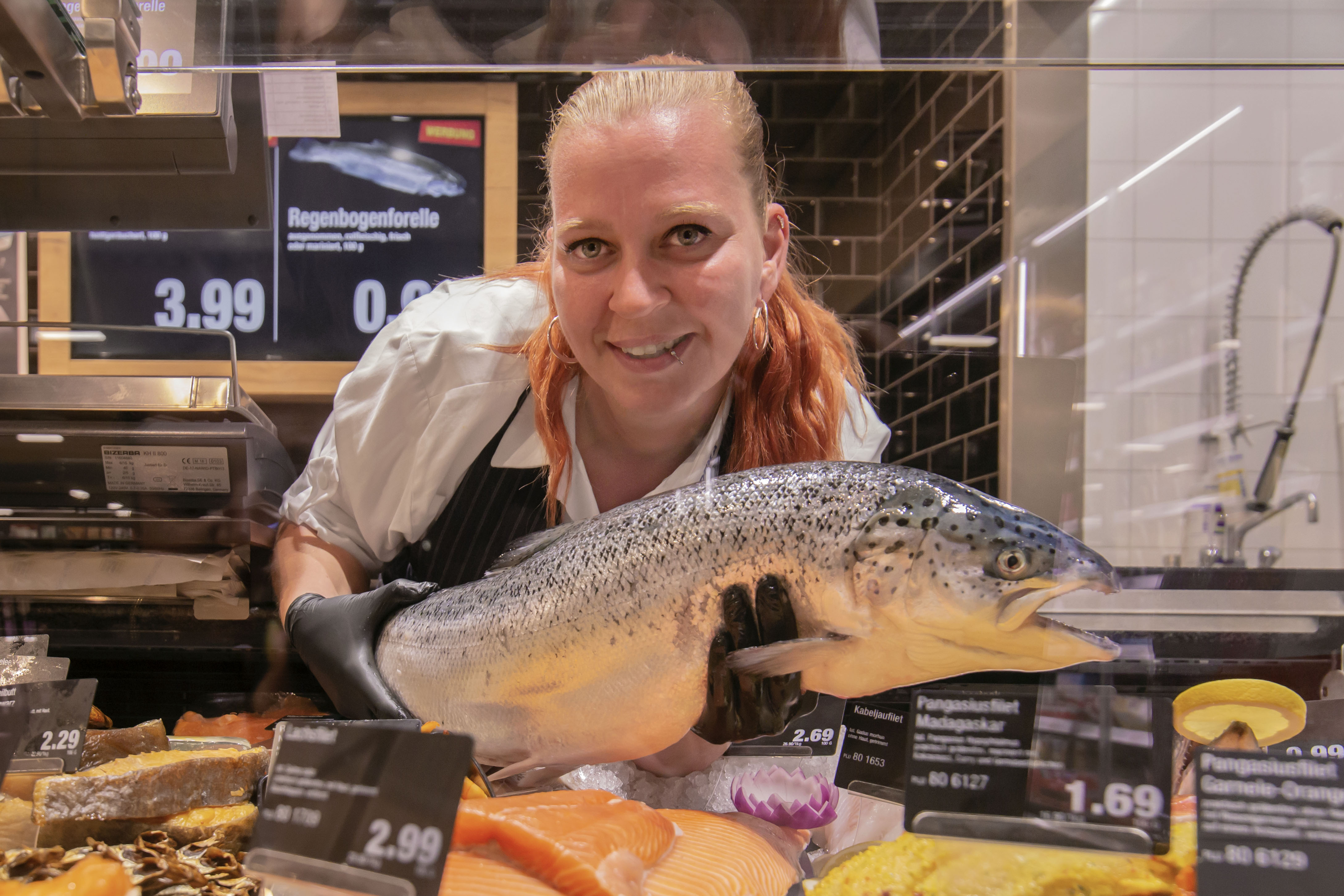 Eine Mitarbeiterin beugt sich zur Kamera herunter und hält einen großen Fisch in beiden Händen.