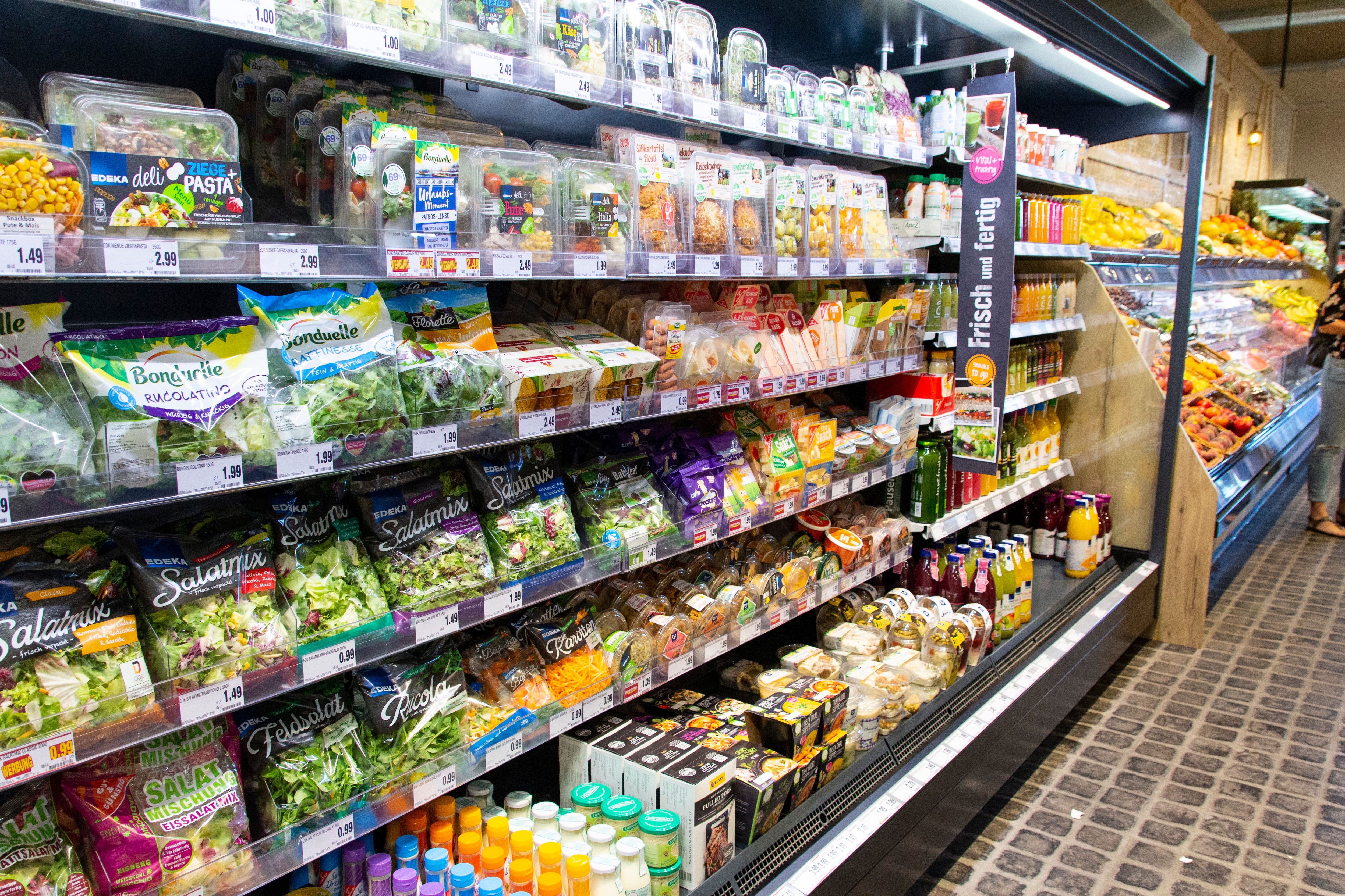 Kühlregal in der Obst- und Gemüseabteilung eines EDEKA-Markts. Darin befinden sich abgepackte Salate und Dressings.